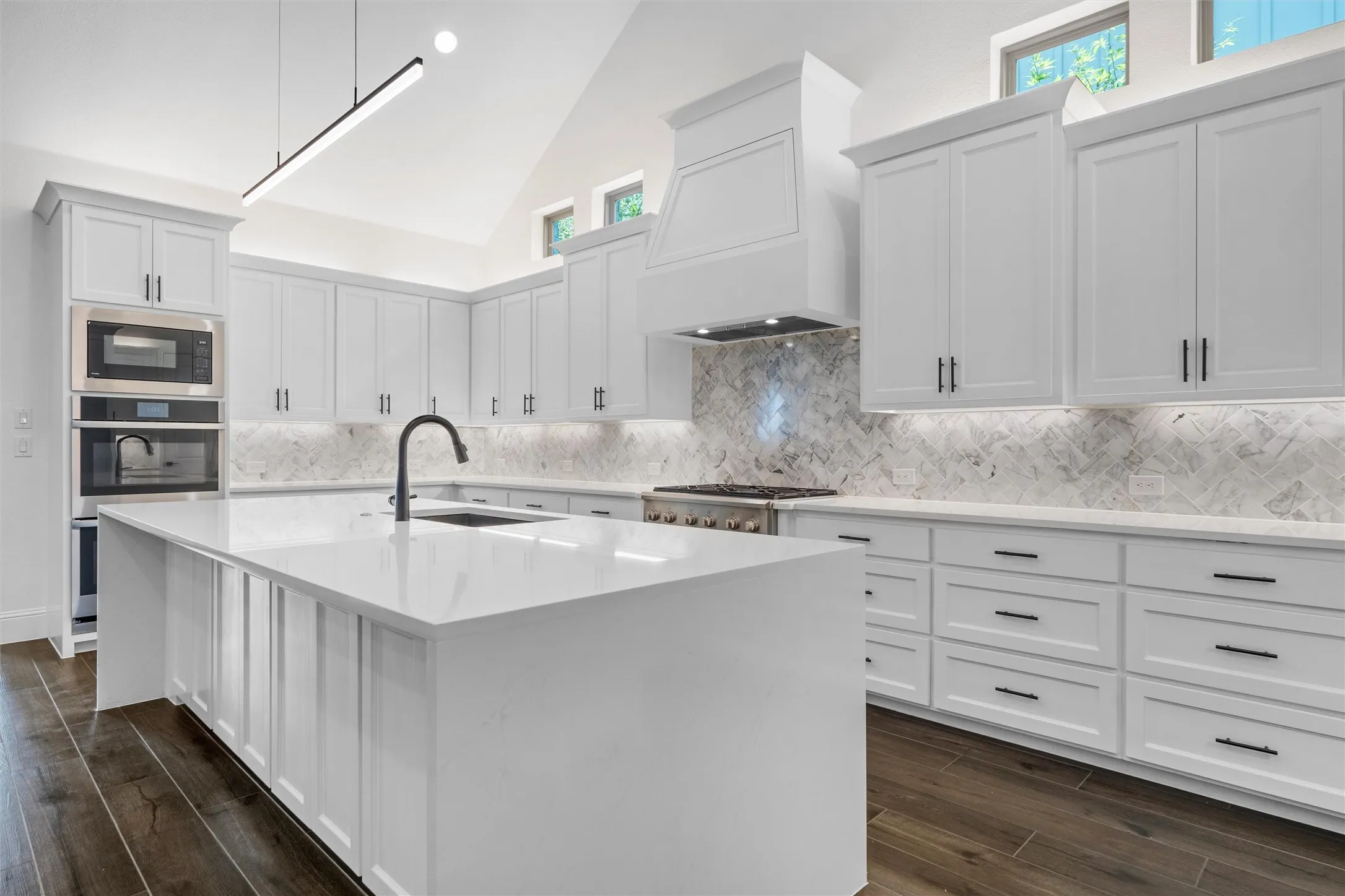 This dream kitchen delivers a clean, modern luxury feel with towering white cabinetry, a dramatic marble-look backsplash, sleek black hardware, and an oversized waterfall-style island made for everything from weekday meals to holiday entertaining.