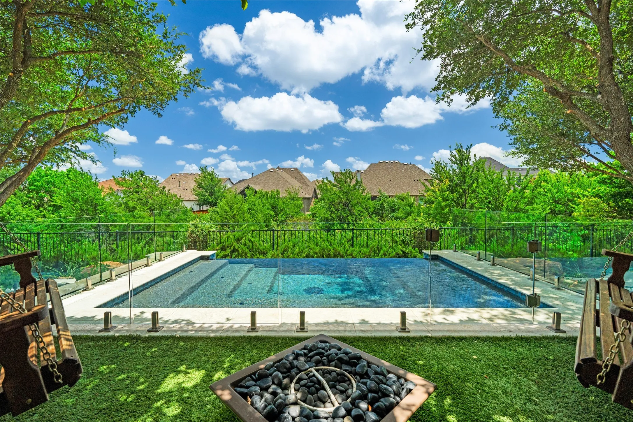 A stunning pool view framed by mature trees, open skies, and glass safety fencing creates a private resort-like atmosphere. The peaceful greenery beyond the pool gives this outdoor space a rare sense of privacy.