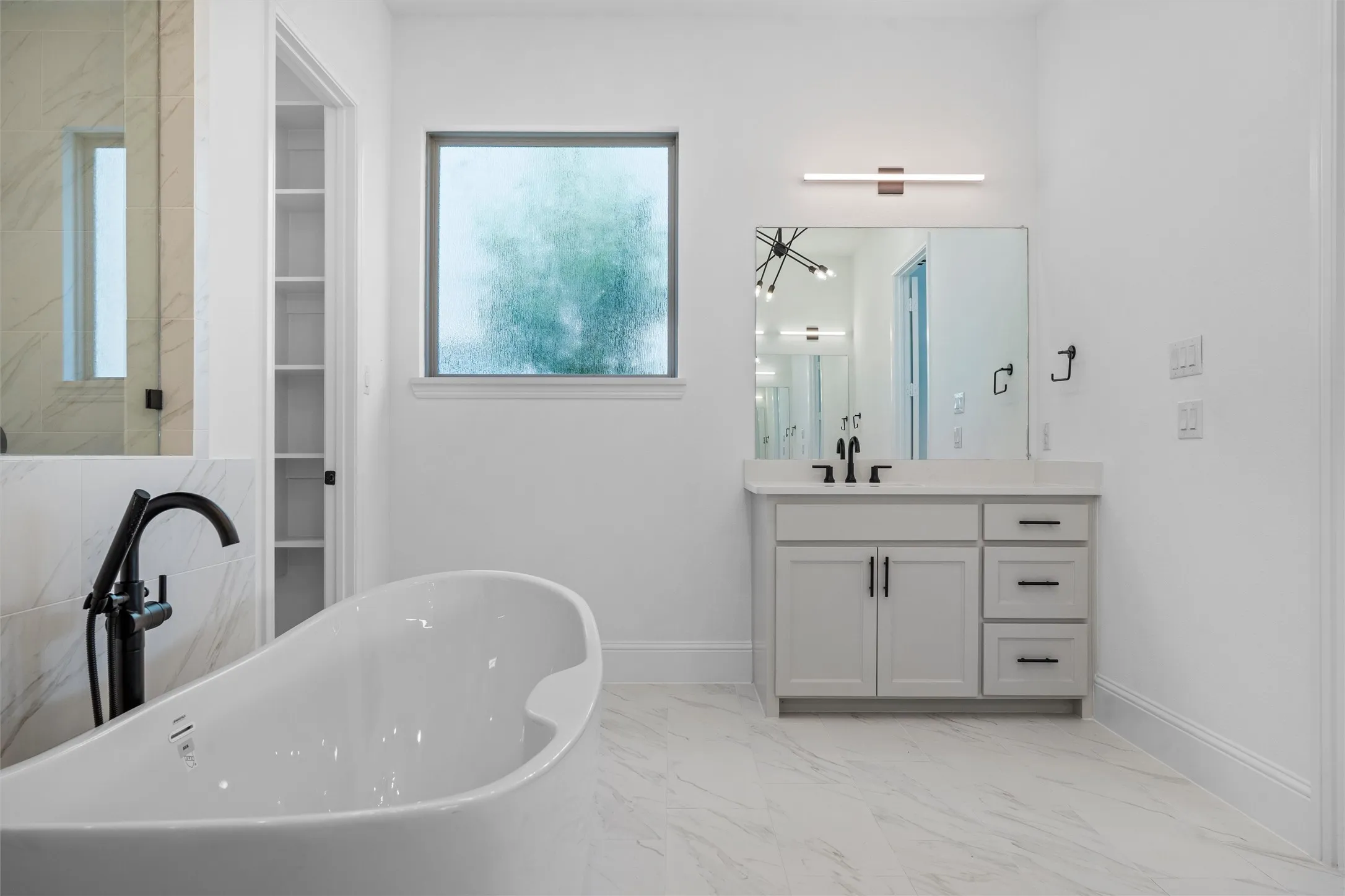 A luxurious bathroom escape featuring a sculptural freestanding soaking tub, sleek black fixtures, marble-style tile, a large vanity, and a frosted window for both natural light and privacy.