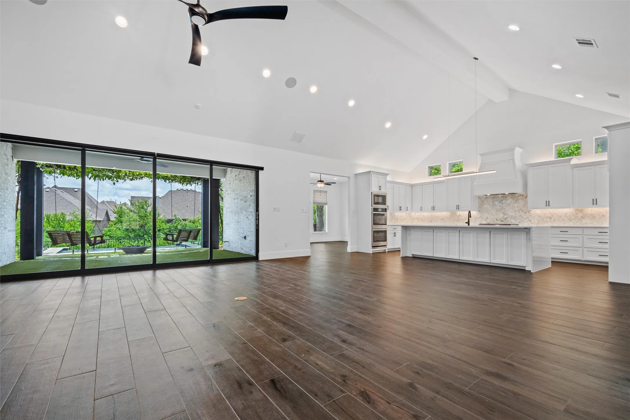 A show-stopping open-concept great room where soaring ceilings, rich wood-look flooring, and a sleek designer kitchen flow effortlessly into the backyard through dramatic sliding glass doors. Built for everyday living and unforgettable entertaining. Enjoy true indoor-outdoor living with a dramatic wall of sliding glass doors opening directly to a covered patio, turf lounge area, and sparkling pool. This is the kind of space made for entertaining, relaxing, and making memories.