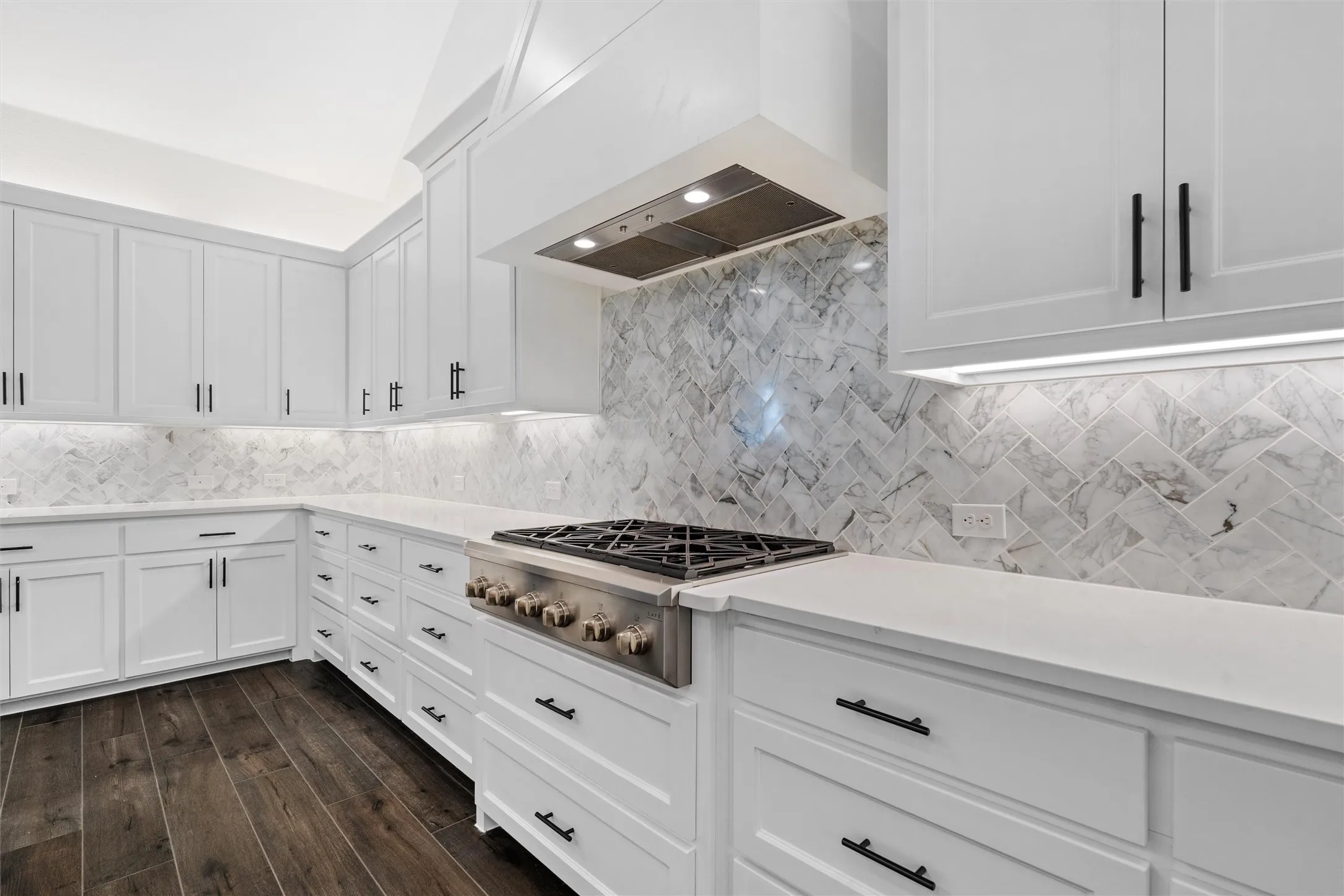 A showpiece cooking wall steals the spotlight with its designer herringbone-style marble backsplash, professional gas range, custom vent hood, and beautifully finished cabinetry—elegant, polished, and built to impress.