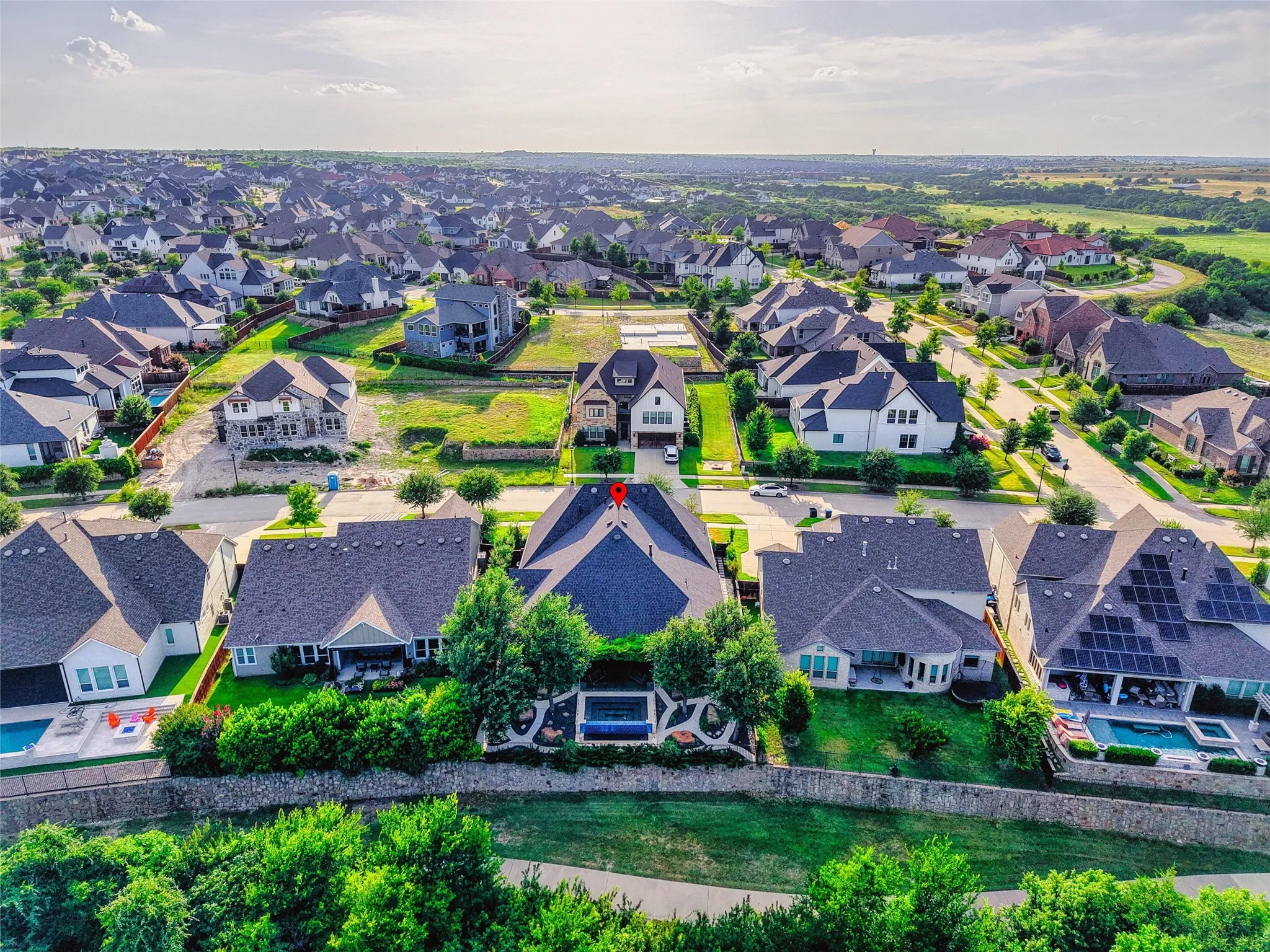 A dramatic aerial view reveals a standout home perfectly positioned along a lush greenbelt backdrop, with a resort-style backyard oasis, stone retaining wall, and scenic trail just beyond the fence line. Surrounded by beautiful homes yet framed by greenery and open views, this is the rare kind of setting that delivers both neighborhood energy and a private escape—luxury living with a view that truly sets it apart.