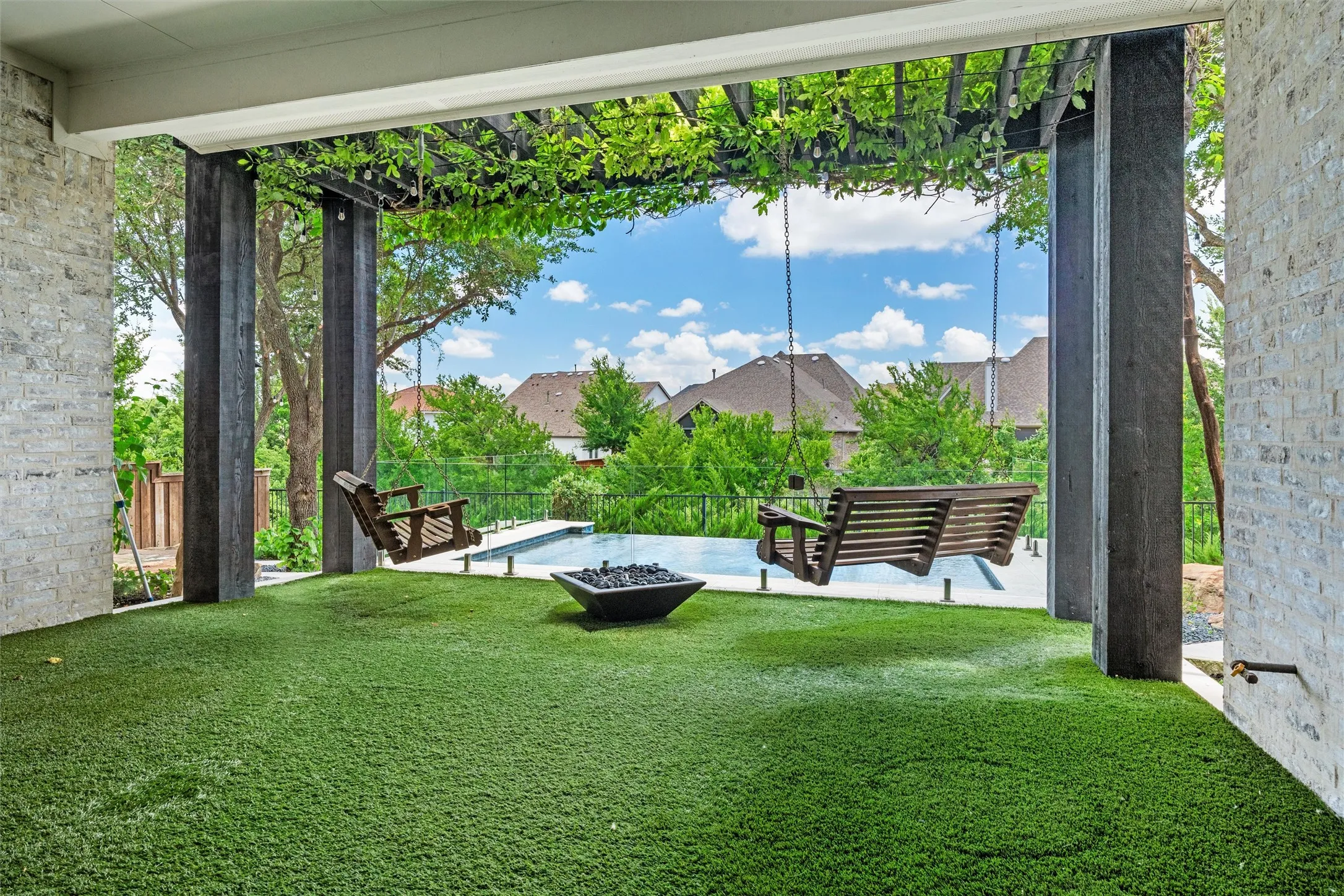 Step into your own backyard retreat featuring covered outdoor living, twin porch swings, a fire feature, lush turf, and a beautiful pool just beyond. The vine-covered pergola adds shade, charm, and a resort-style feel.