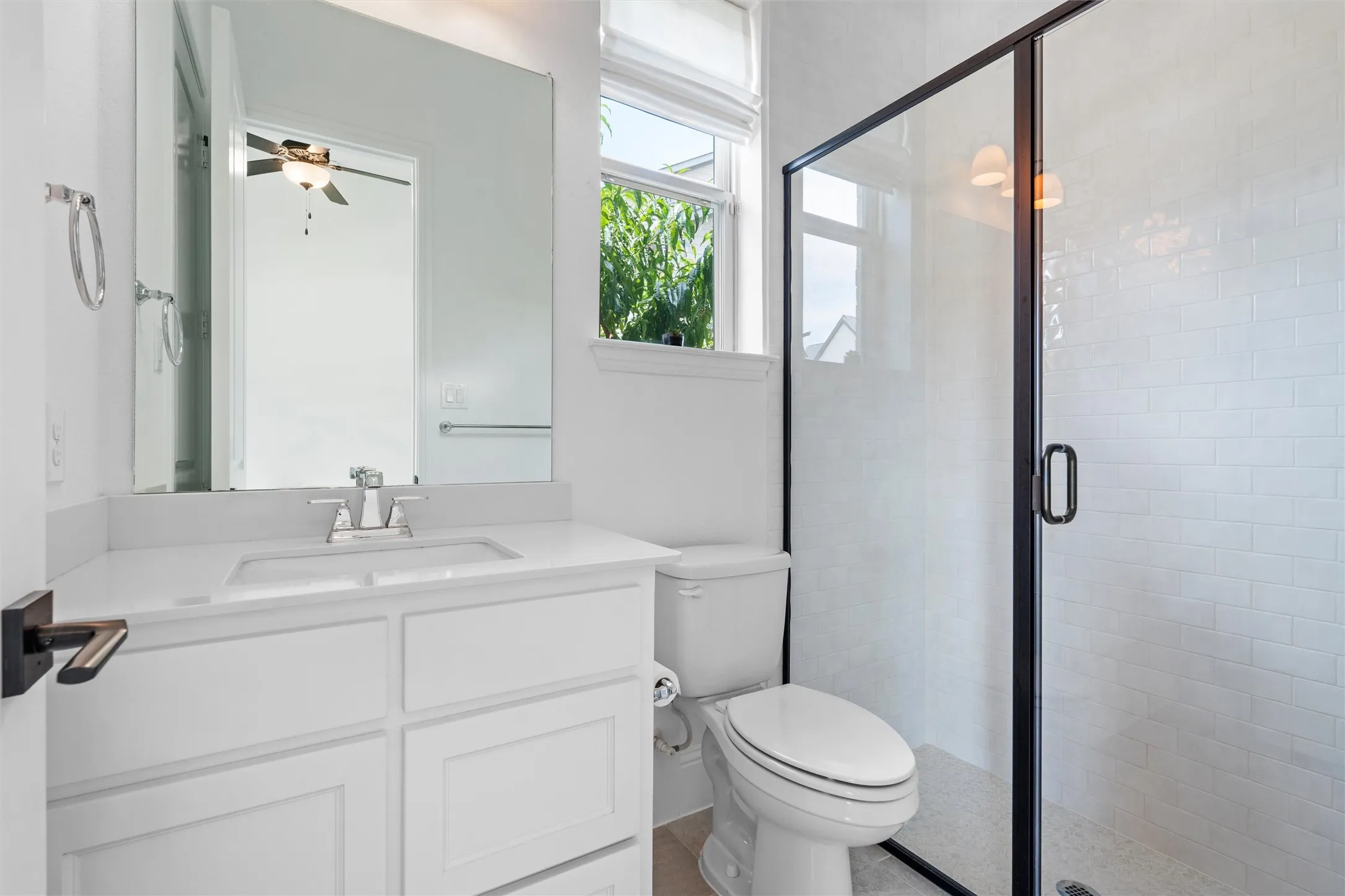 This stylish ensuite bath pairs crisp white cabinetry with a sleek black-framed glass shower, subway tile surround, and natural light for a fresh, modern finish.