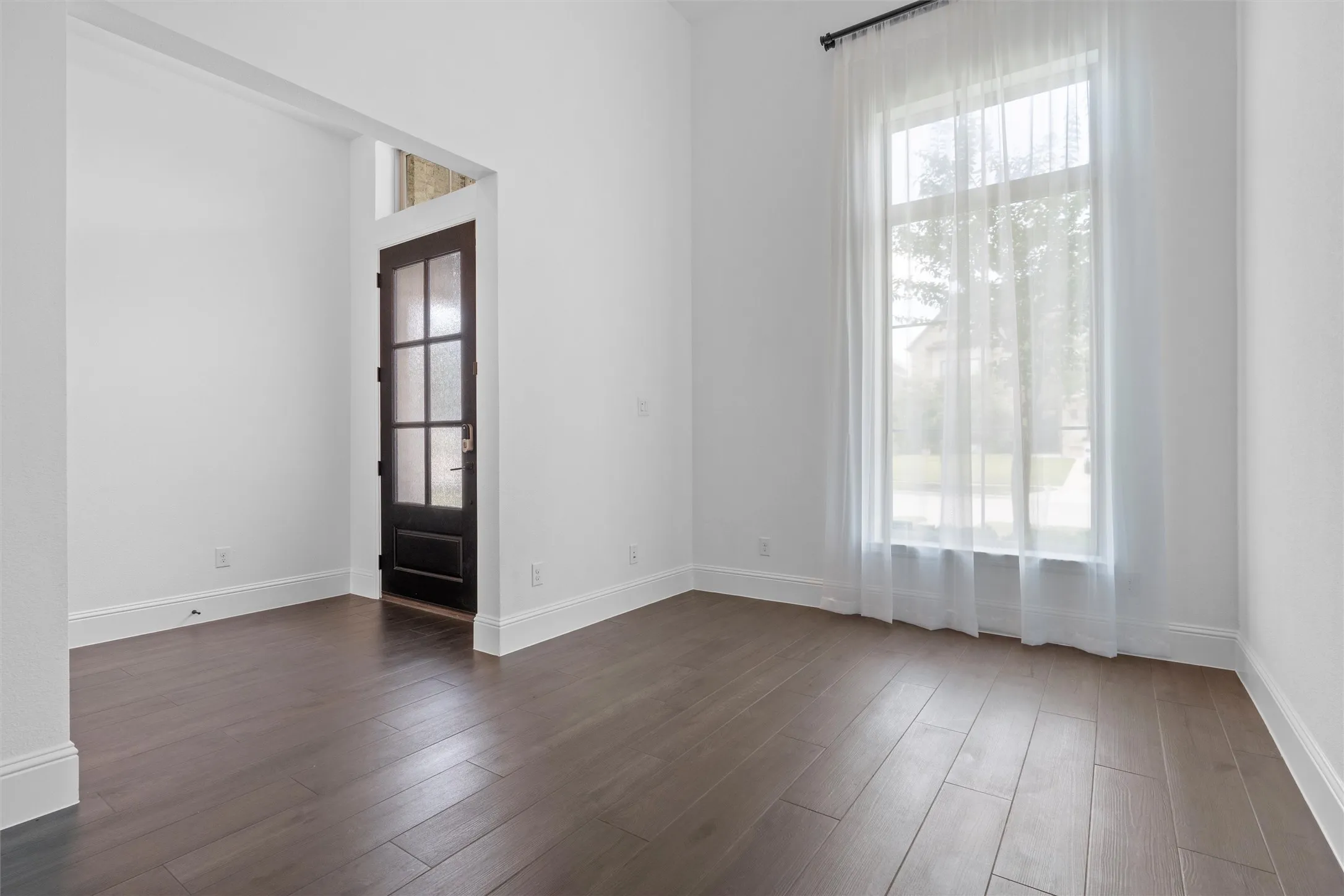 This bright front flex room is ready to become your dream home office, formal sitting area, reading lounge, or creative studio, with tall windows, soft natural light, and a welcoming view of the entry.