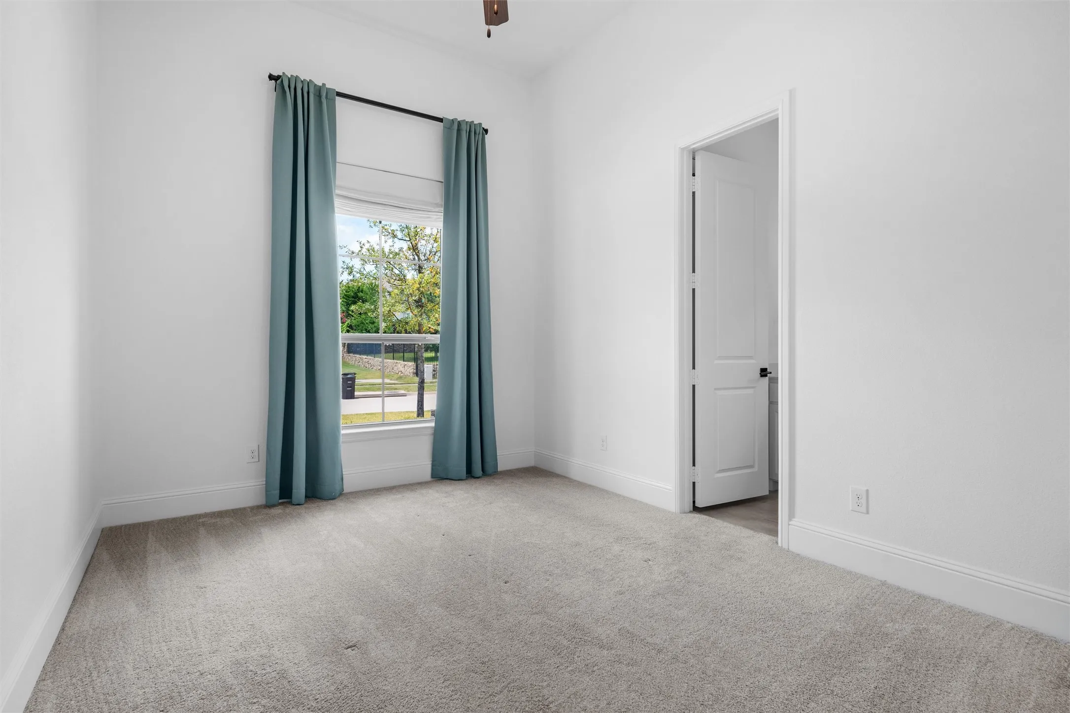 A bright and inviting secondary bedroom with soft carpeting, a large window, and a clean neutral palette ready for a child’s room, guest suite, or home office.