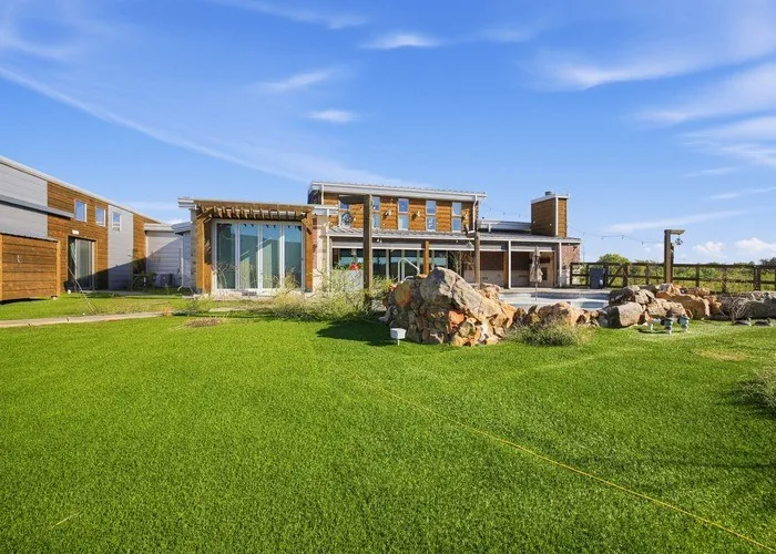 Expansive manicured lawn with mature landscaping, complemented by modern architectural design featuring wood-finish exterior cladding, large multi-pane windows, and contemporary mixed-material construction