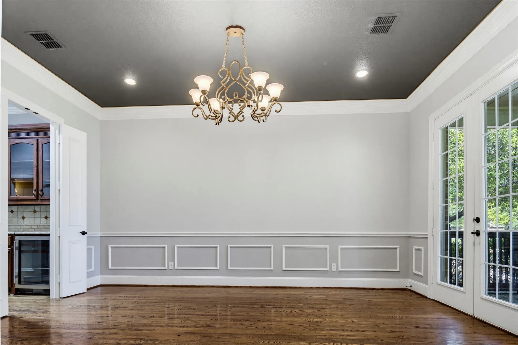Dining Room features wainscoting and french doors to patio! A stately chandelier is the gorgeous focal point in this room. Adjoining butler's pantry provides storage as well as space for serving a buffet.