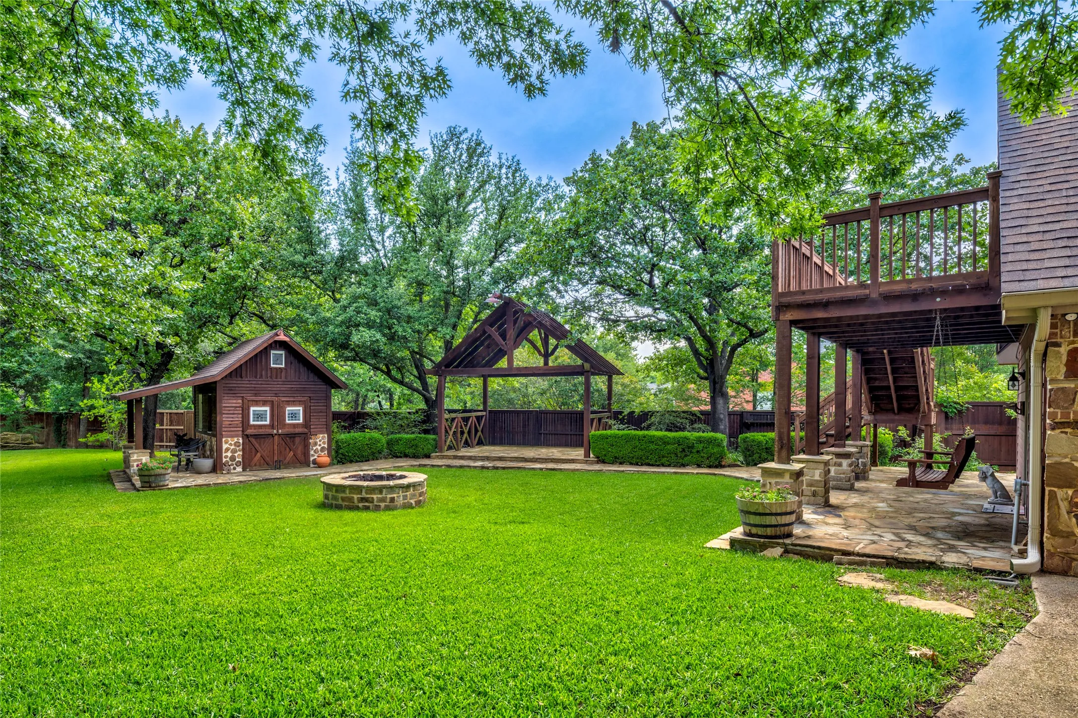 This photo shows the outdoor stage, firepit, and quaint cabin storage shed. Also shown is the patio and deck leading to the storage room above the 3 car detached garage.