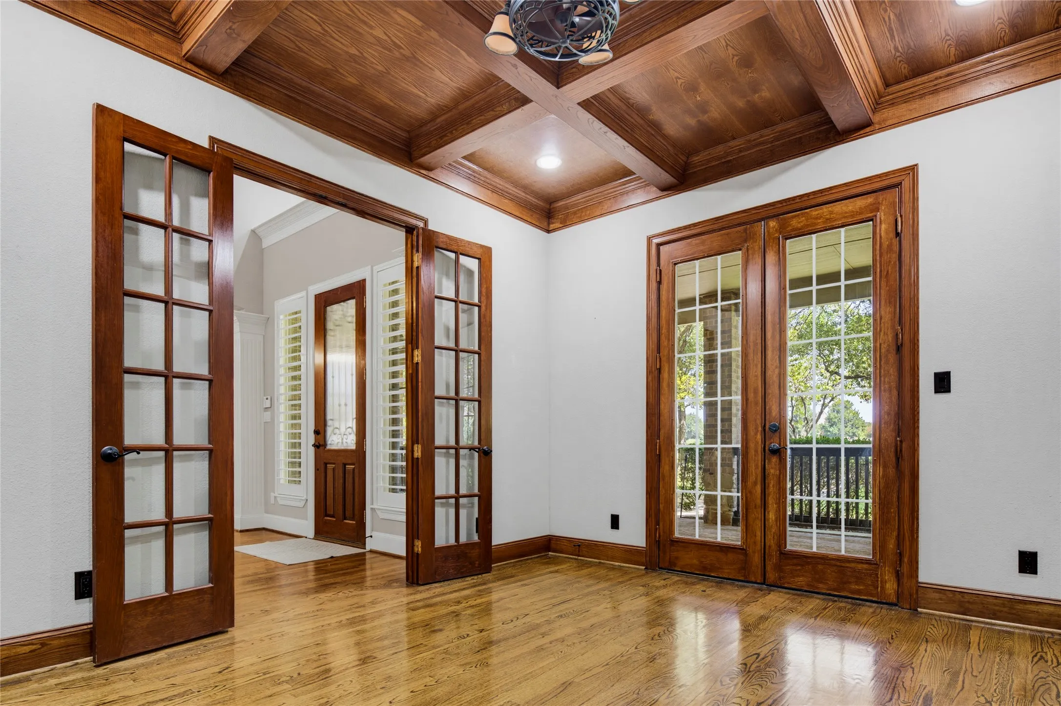 Designated office with french doors & coffered ceiling has views of the beautiful front yard. A second set of french doors open to the covered front porch. Another door (on wall not shown in pic) opens to the primary closet for storage and easy access to the primary suite.