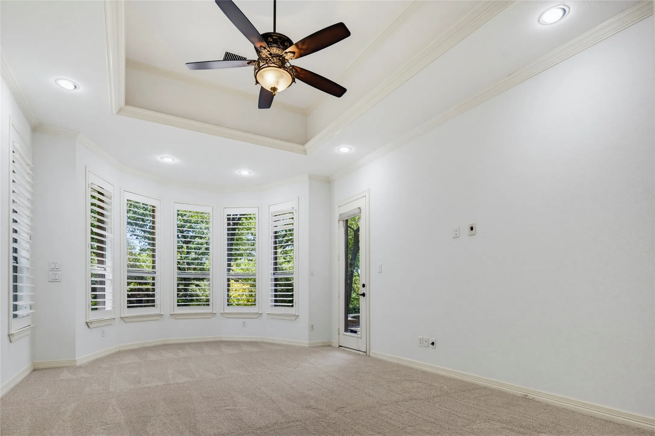 The primary bedroom features bay windows with plantation shutters, a tray ceiling, and a private door leading to the back patio. Very spacious at 18' x 14'.