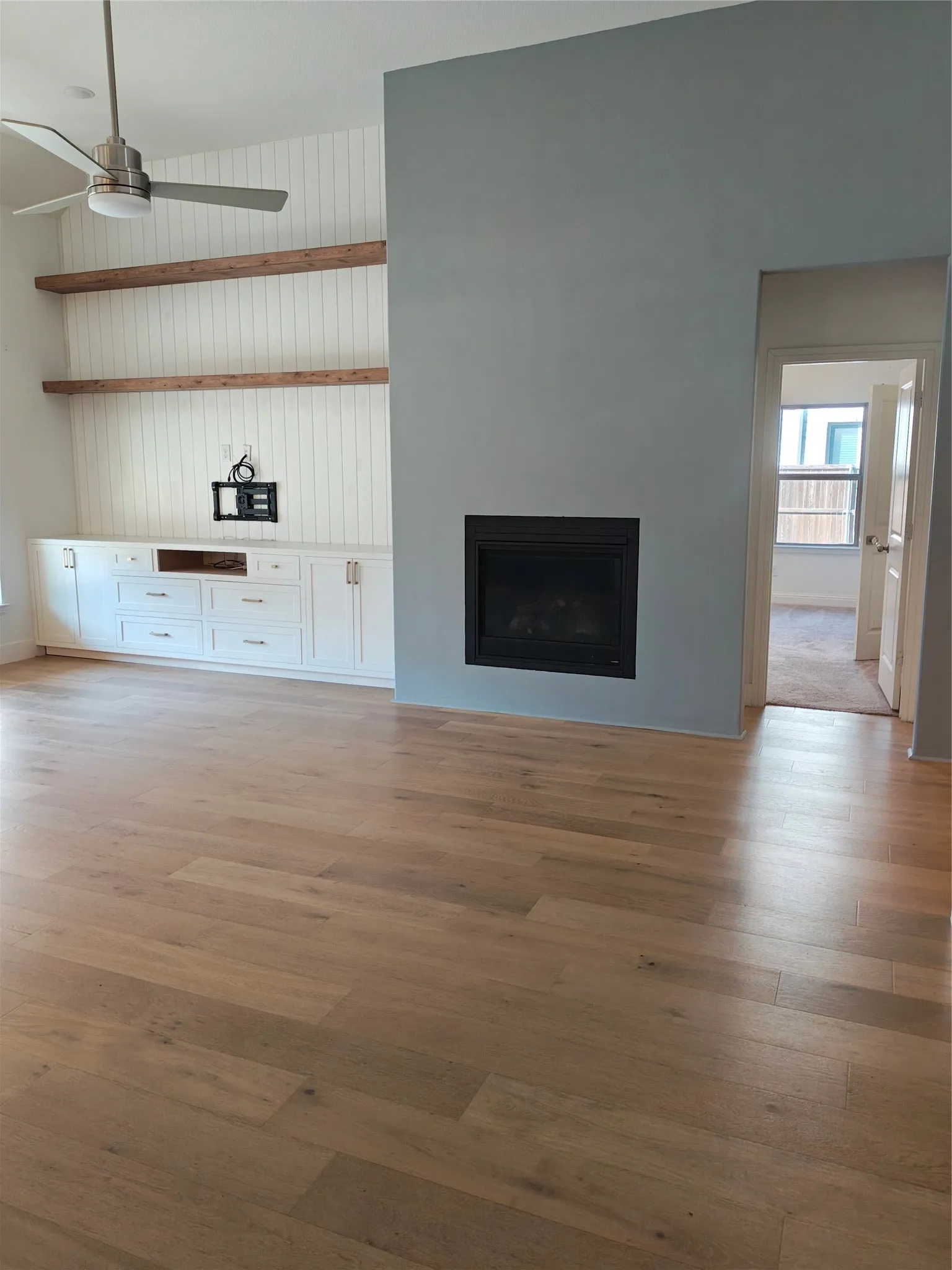 Wide plank wood-finish flooring, built-in fireplace, recessed shelving, built-in cabinetry, and a ceiling fan with integrated lighting