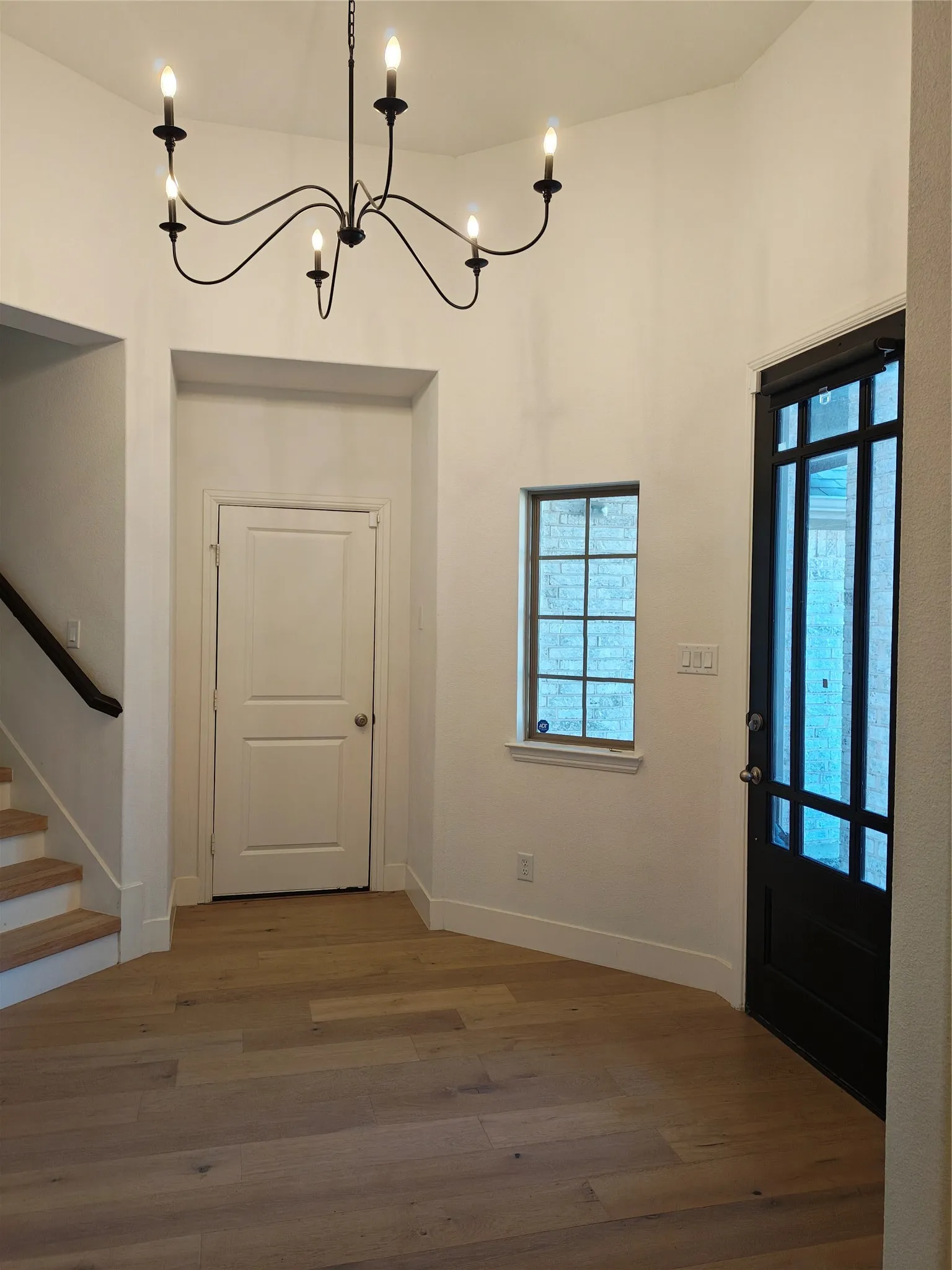 Engineered wood flooring, black wrought iron chandelier, paneled interior door, black framed window, and a black front door with multiple lites