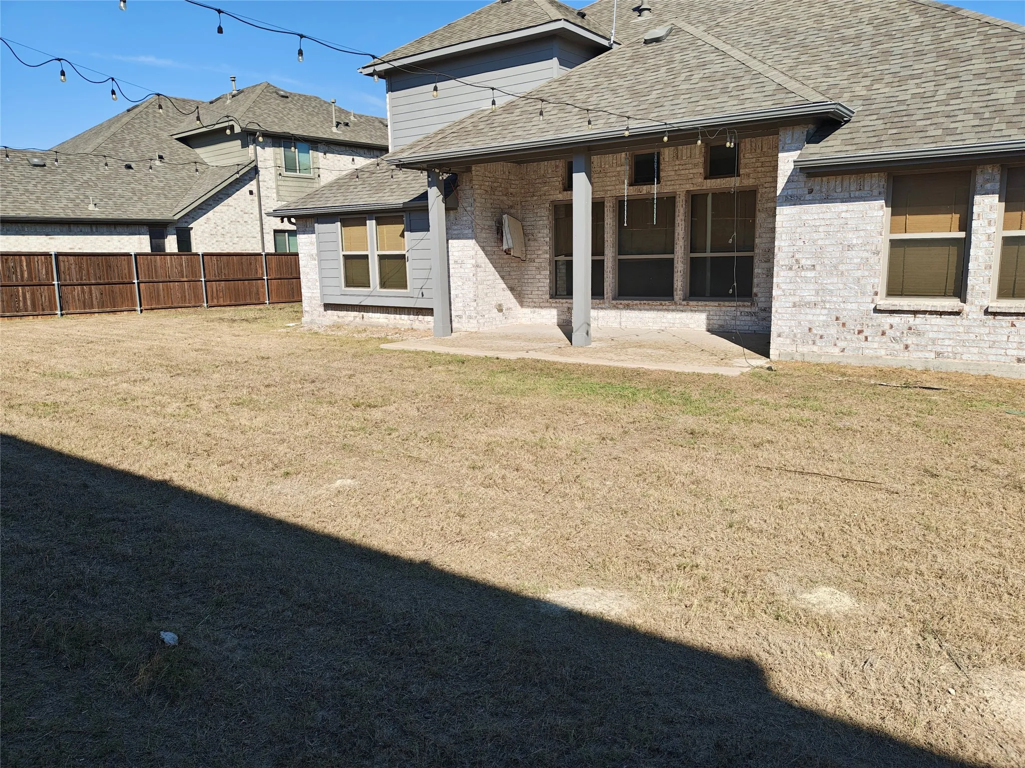 Expansive backyard featuring a privacy fence, covered patio, and string lighting