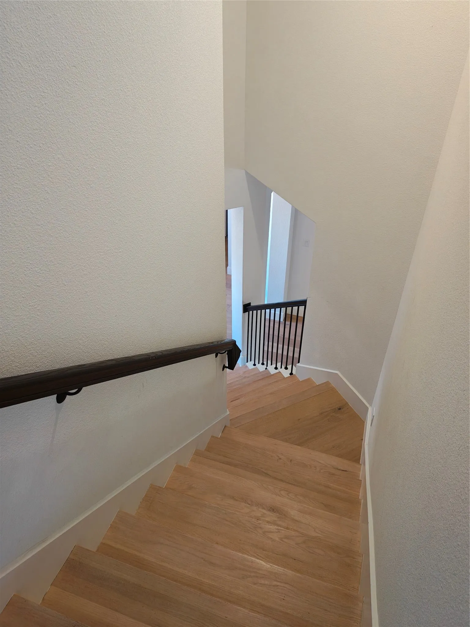 Hardwood staircase with a dark wood handrail and wrought iron balusters