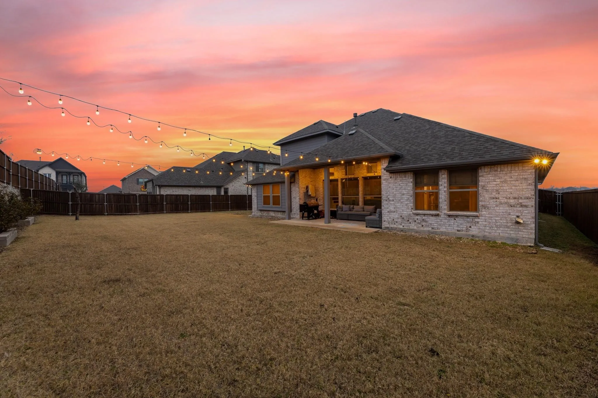 Expansive backyard featuring a covered patio, string lights, and a full privacy fence