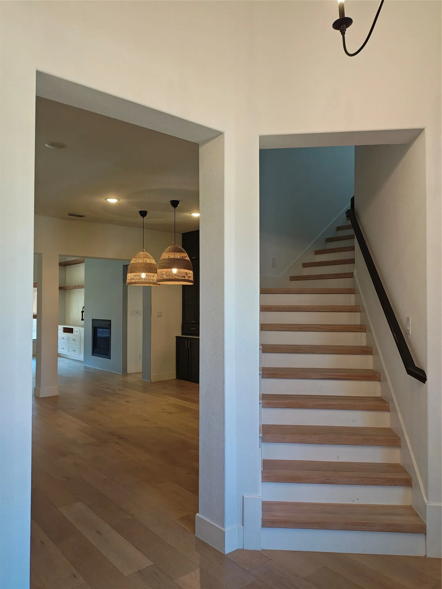 Hardwood flooring, painted risers, modern black handrail, recessed lighting, and woven pendant light fixtures