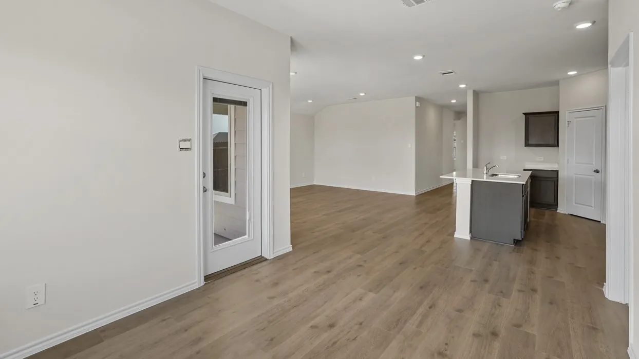 Spacious open-concept interior featuring light gray walls, wood-finish flooring, recessed lighting, and a modern kitchen island with a double basin sink