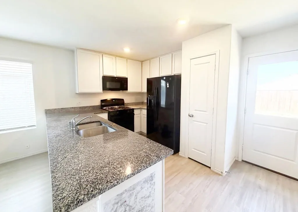 Kitchen featuring light wood-finish flooring, white cabinetry, and granite-style countertops