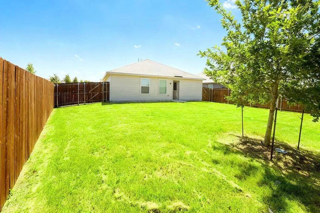 Expansive backyard featuring a lush lawn, privacy fencing, and a mature tree