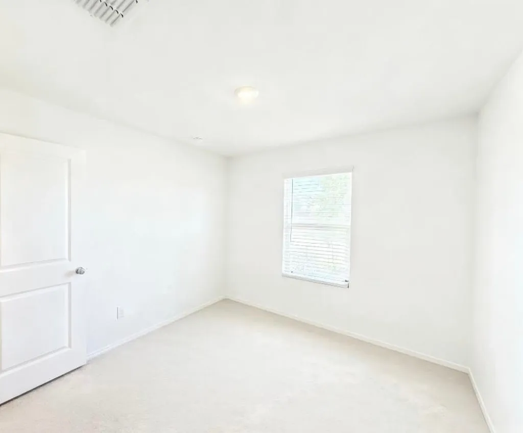 Bright room featuring a window with blinds, light-colored carpeting, a white interior door, and a ceiling-mounted light fixture
