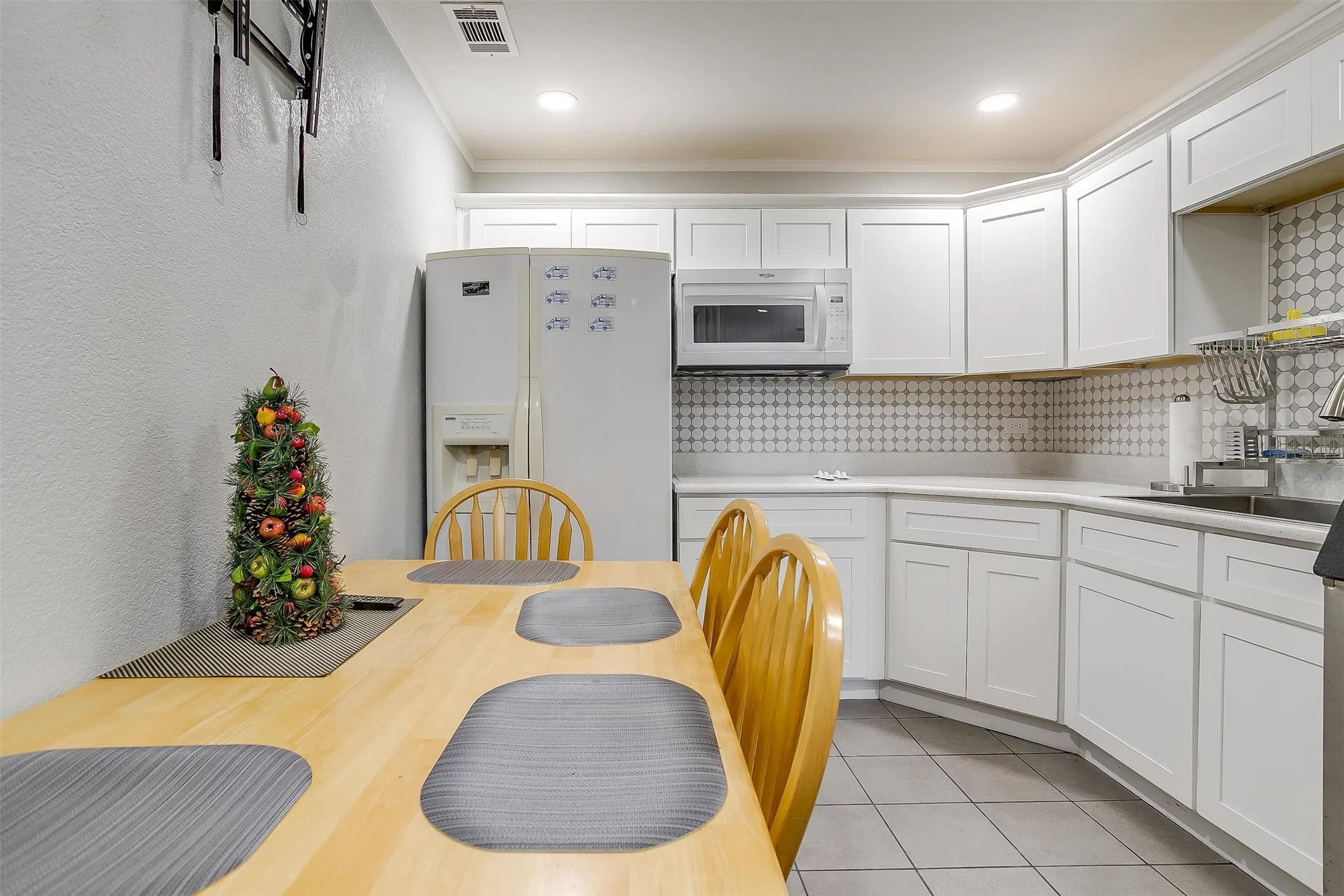 Modern kitchen featuring white shaker cabinetry, patterned tile backsplash, stainless steel microwave, and a double basin sink