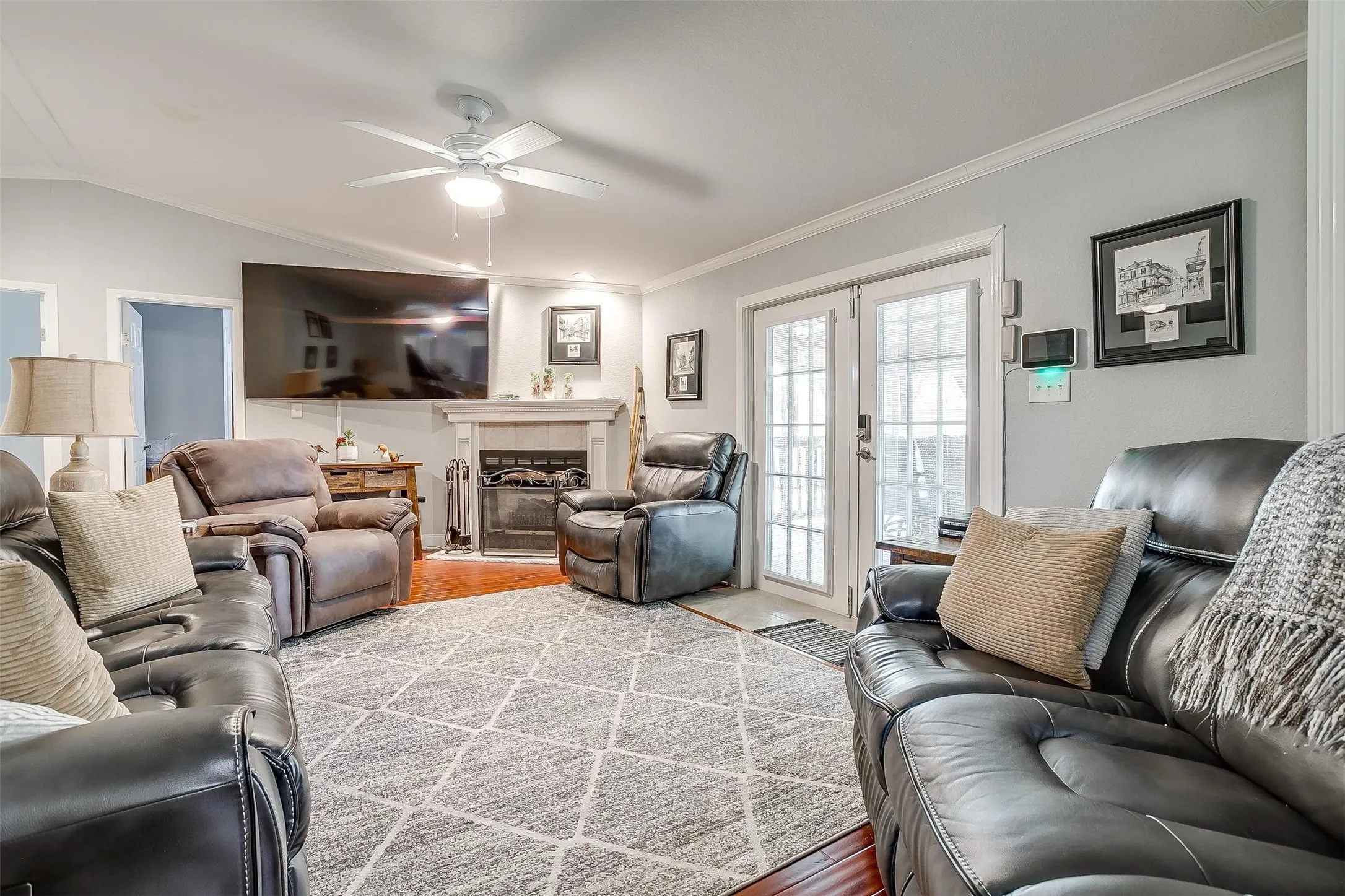 Living area featuring wood-finish flooring, a ceiling fan with integrated lighting, a fireplace with a stone surround, and French doors