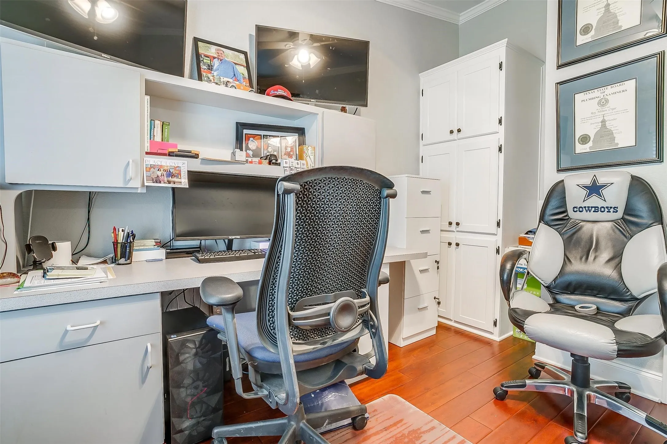 Dedicated office space featuring built-in cabinetry, engineered wood flooring, wall-mounted display screens, and crown molding