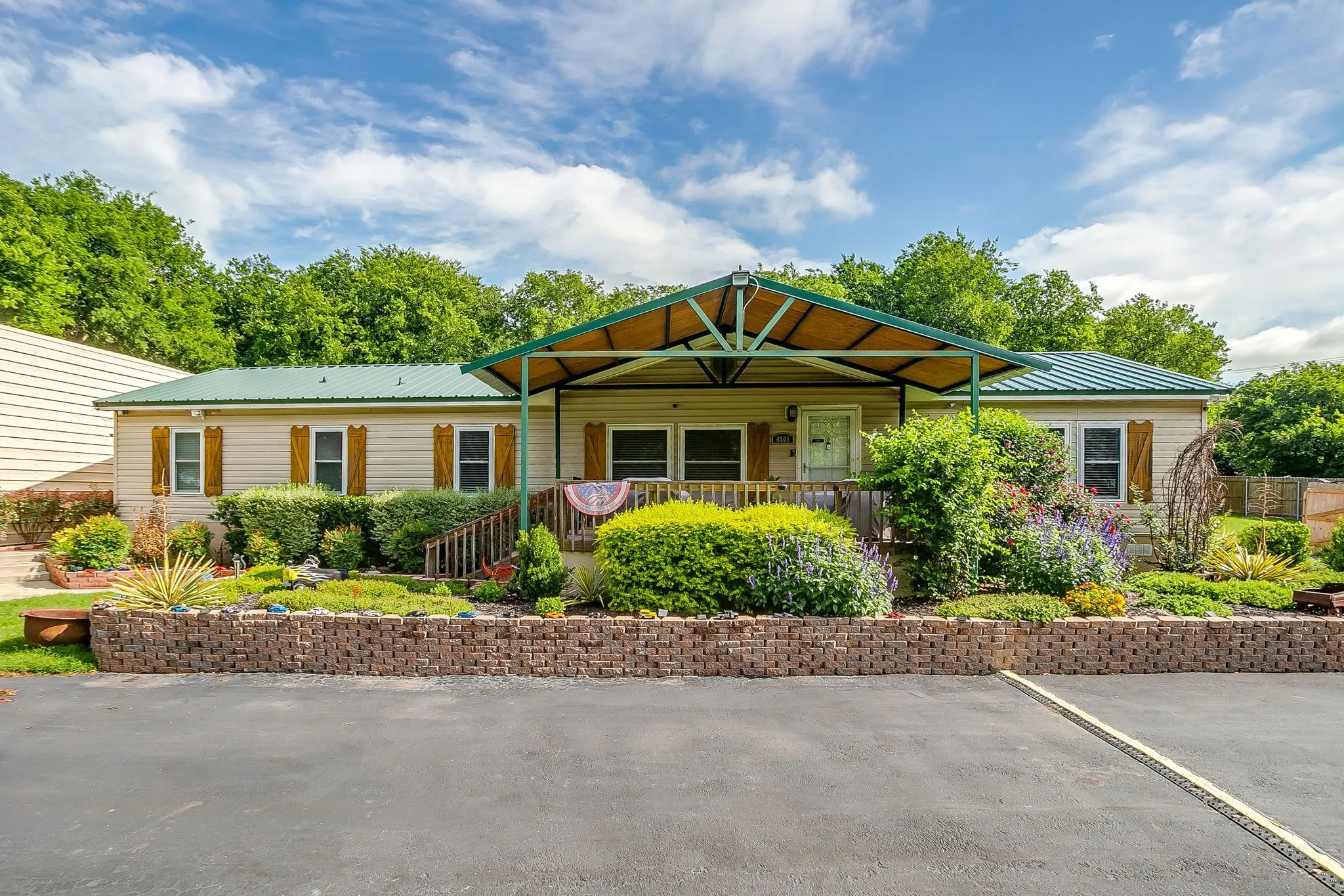 Residence with beige siding and a green metal roof, featuring a covered front porch with a wood deck and steps
