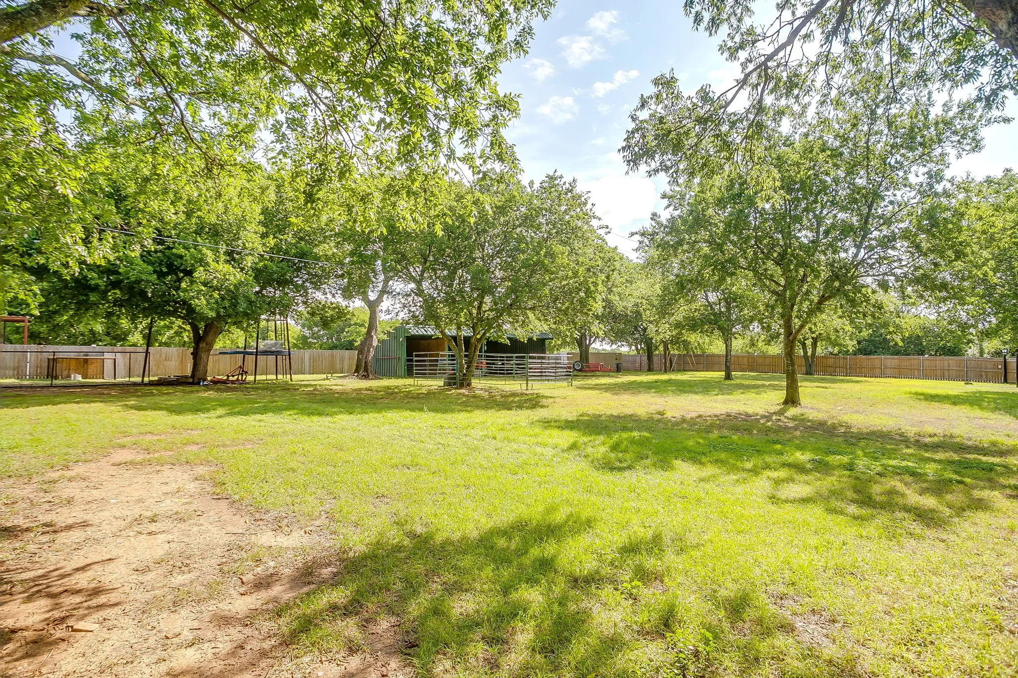 Expansive grassy area featuring mature trees and a perimeter wood fence