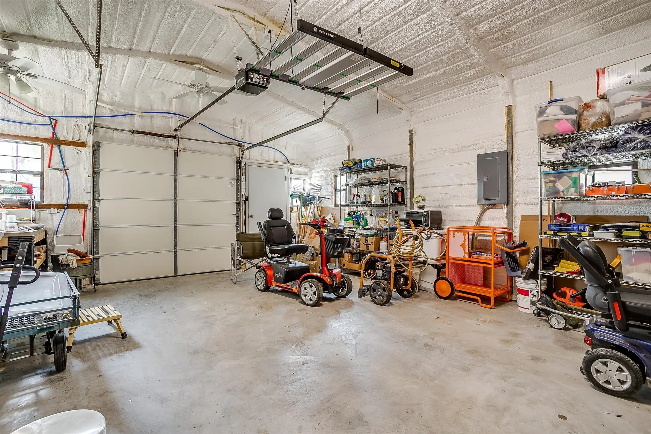 Spacious garage featuring a large overhead door, concrete flooring, and ceiling fans for air circulation