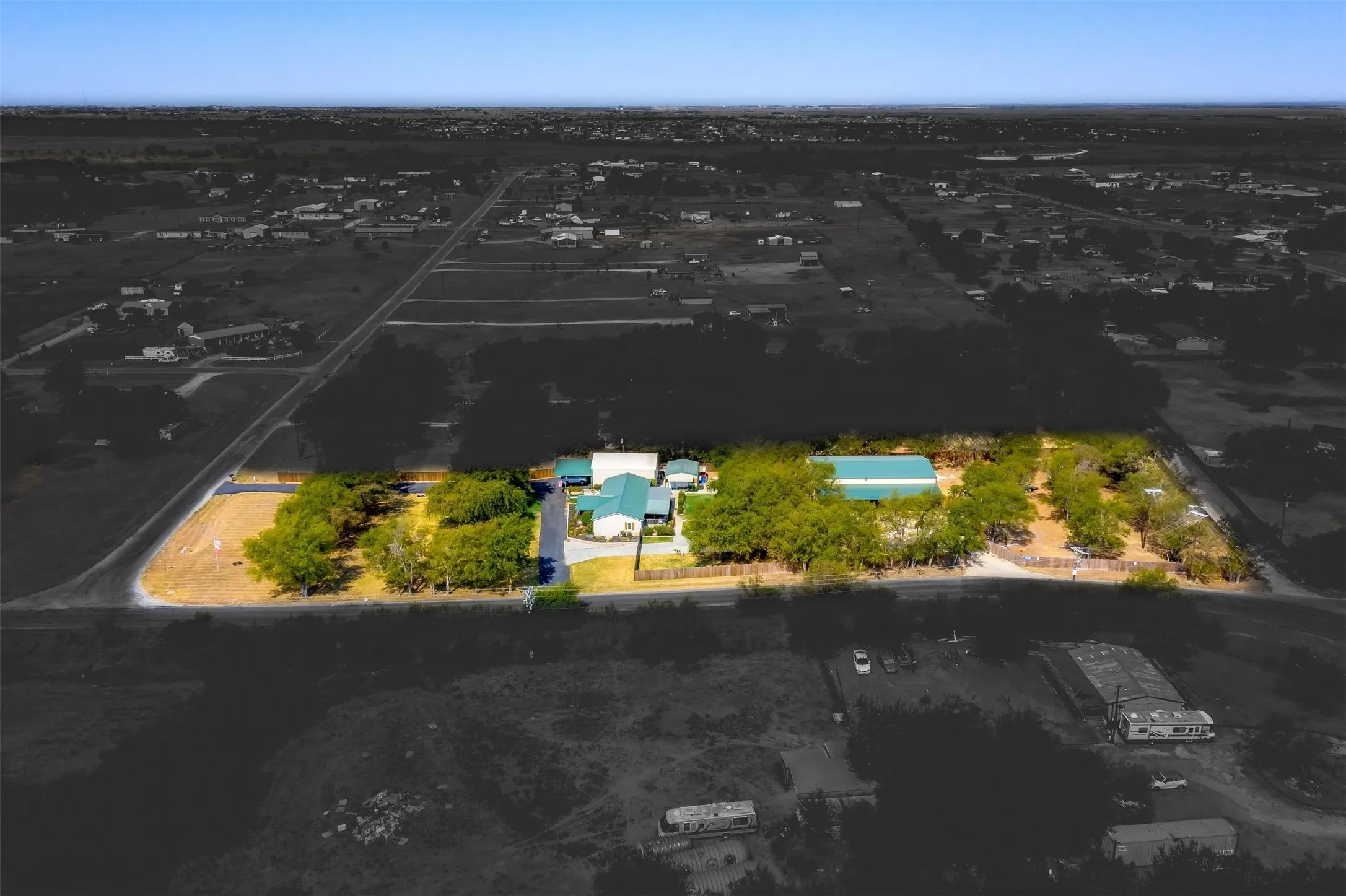 Expansive property featuring multiple buildings, mature trees, a gravel driveway, and a large metal-roofed structure