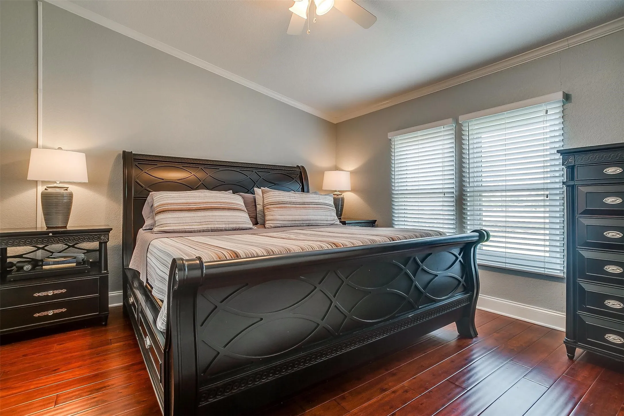 Bedroom featuring wood-finish flooring, light grey walls, white crown molding, and two windows with blinds