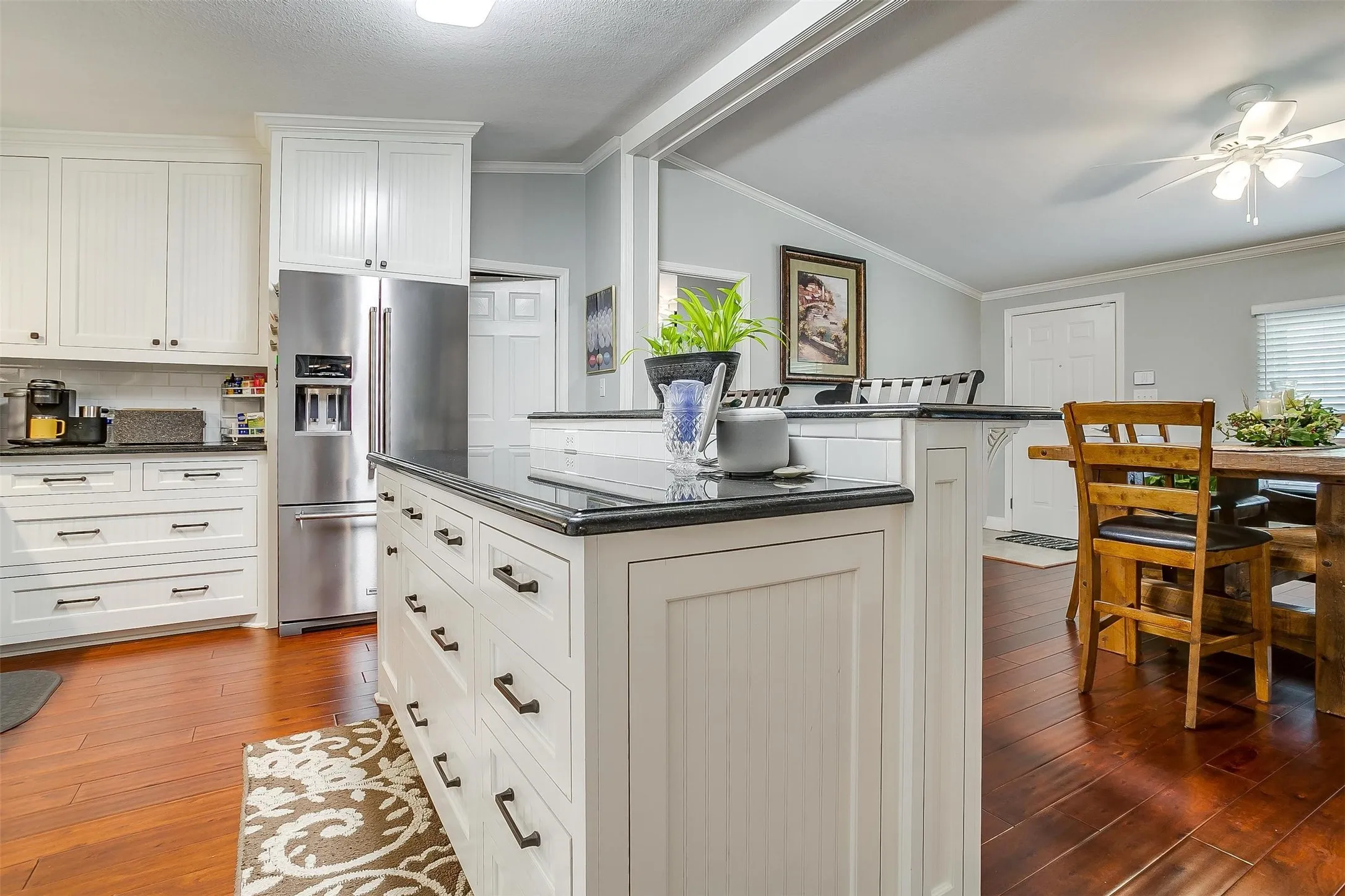 Kitchen with white shaker-style cabinetry, dark countertops, a large center island, stainless steel refrigerator, and wood-finish flooring