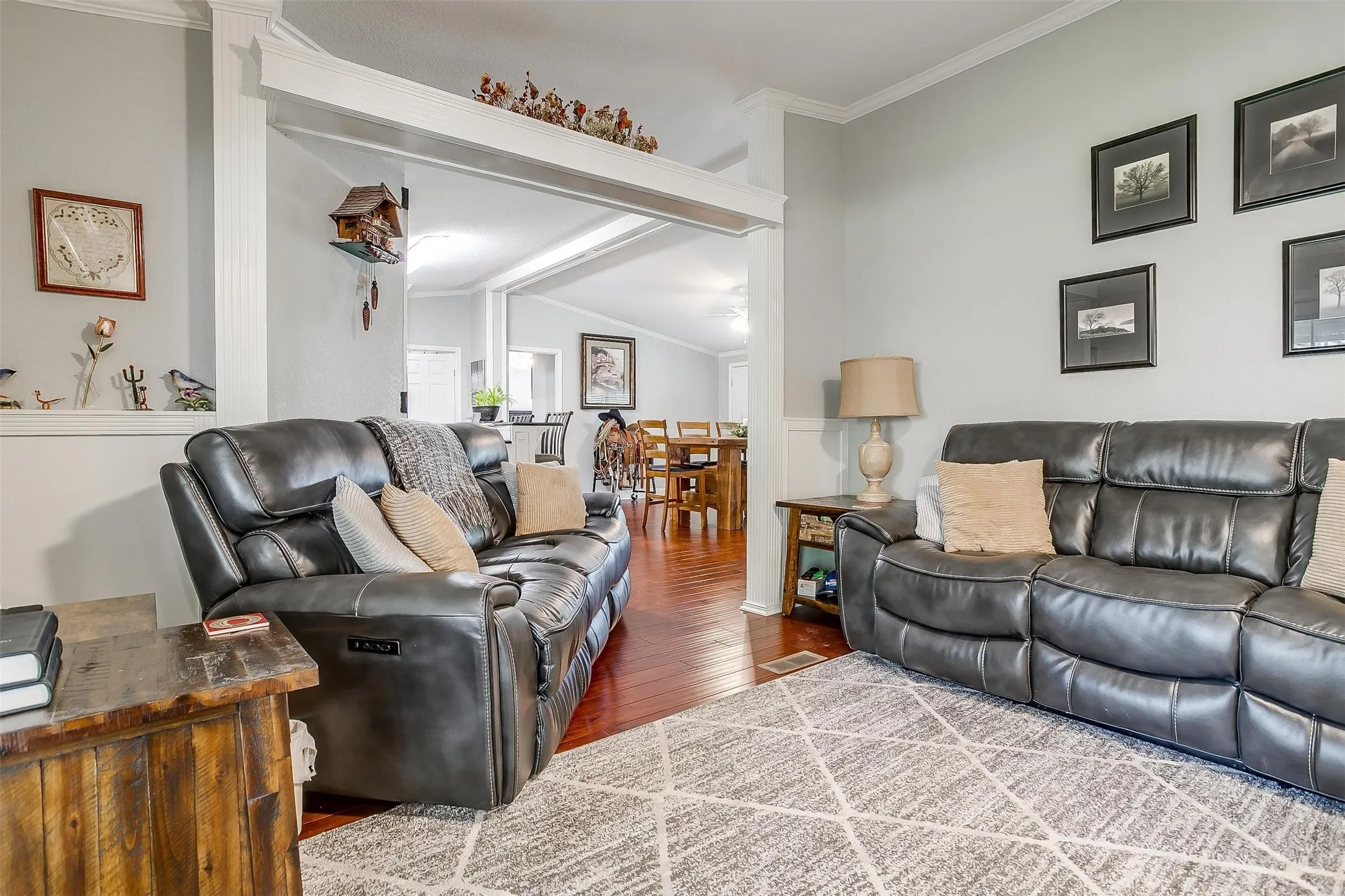 Open-concept living area featuring light gray walls, white crown molding, wood-finish flooring, and a decorative archway