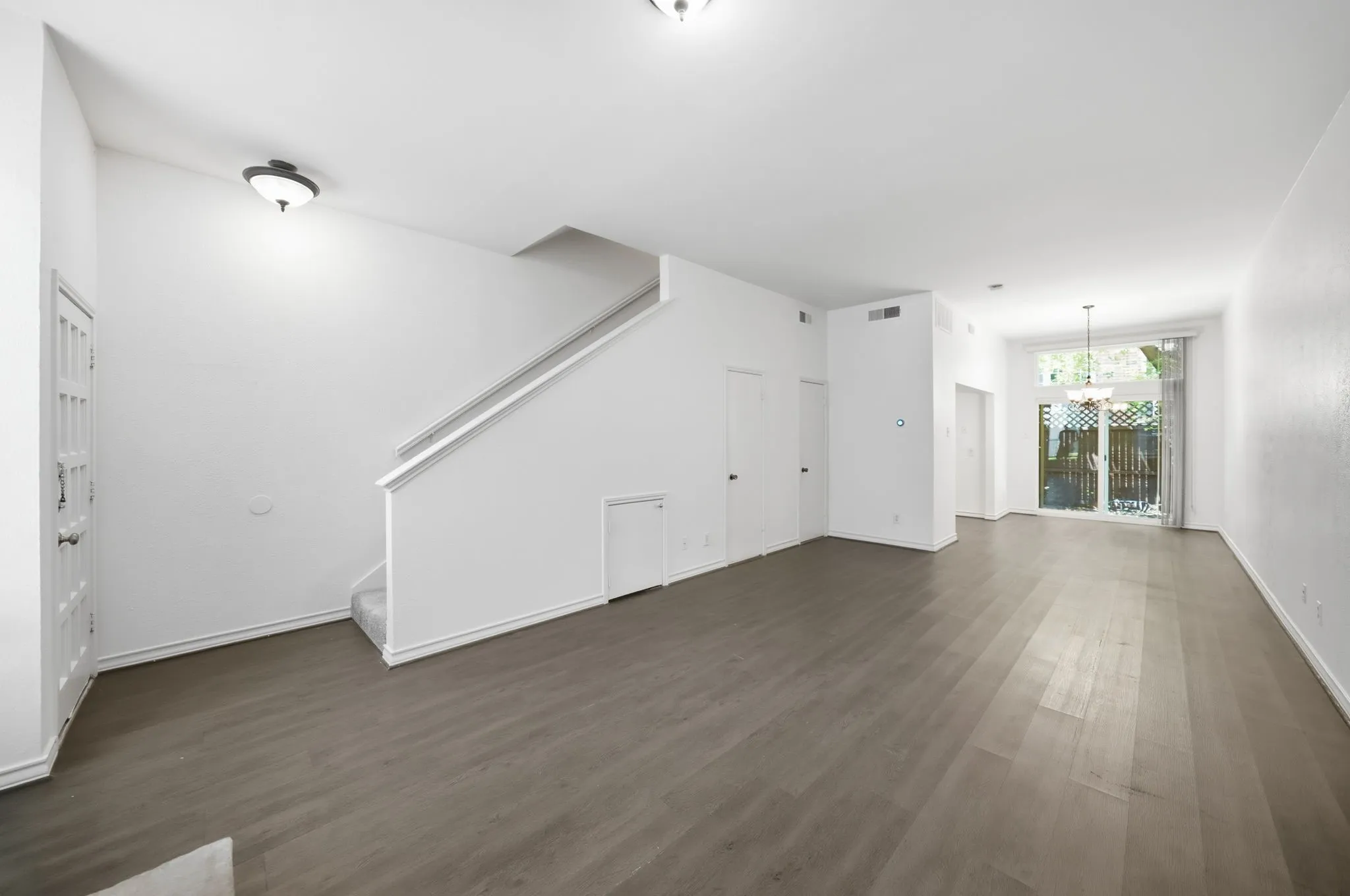 Open-concept living area with wood-finish flooring, a contemporary staircase, and clean white walls