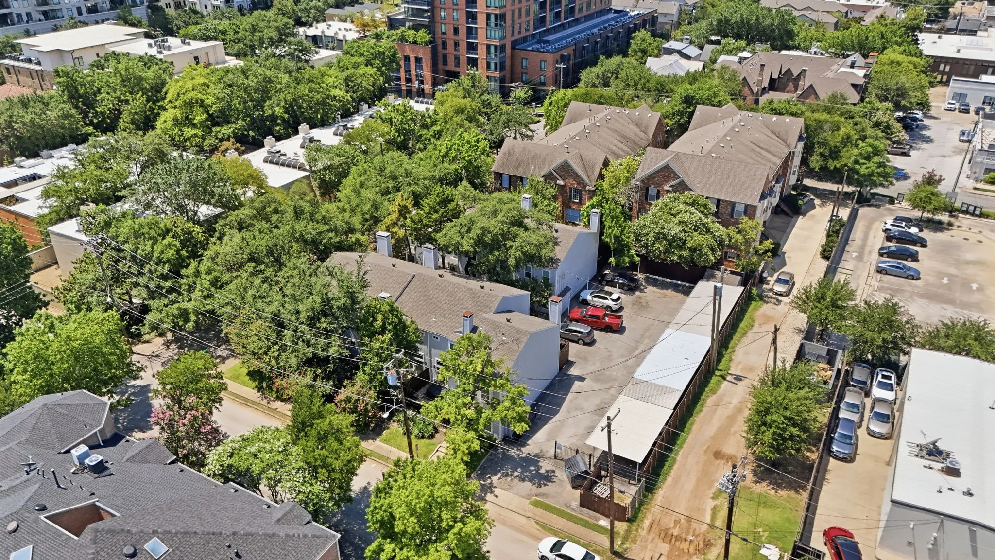 Multiple residential structures with brown shingle roofing and brick facades surrounded by mature trees