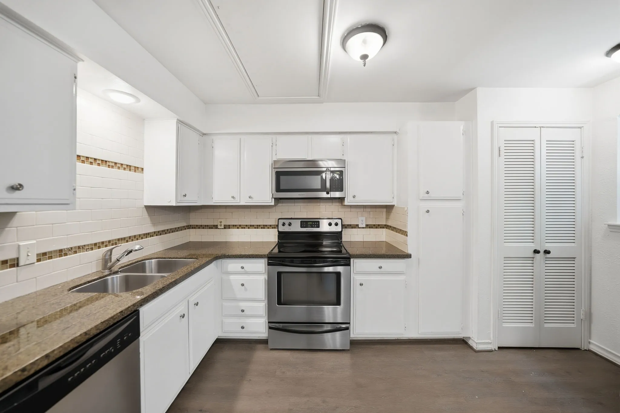 Kitchen featuring white cabinetry, stainless steel appliances, granite-look countertops, subway tile backsplash with decorative accent, and a dual basin sink