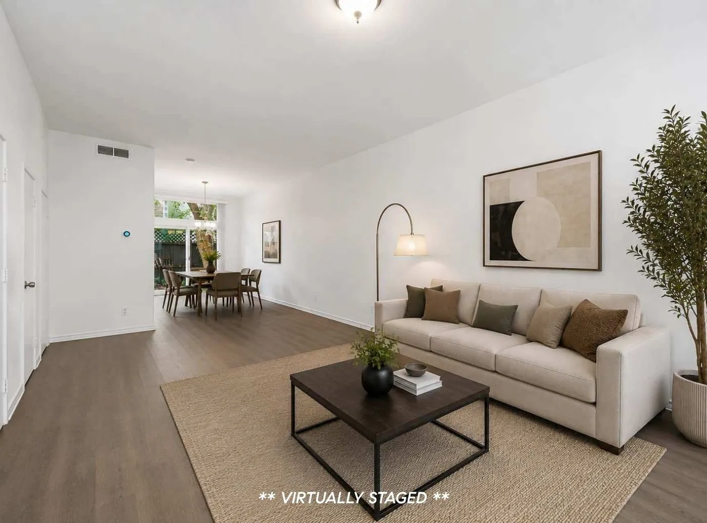 Open-concept living area featuring wood-finish flooring throughout, a dining space with natural light, a window overlooking exterior greenery, and clean white walls
