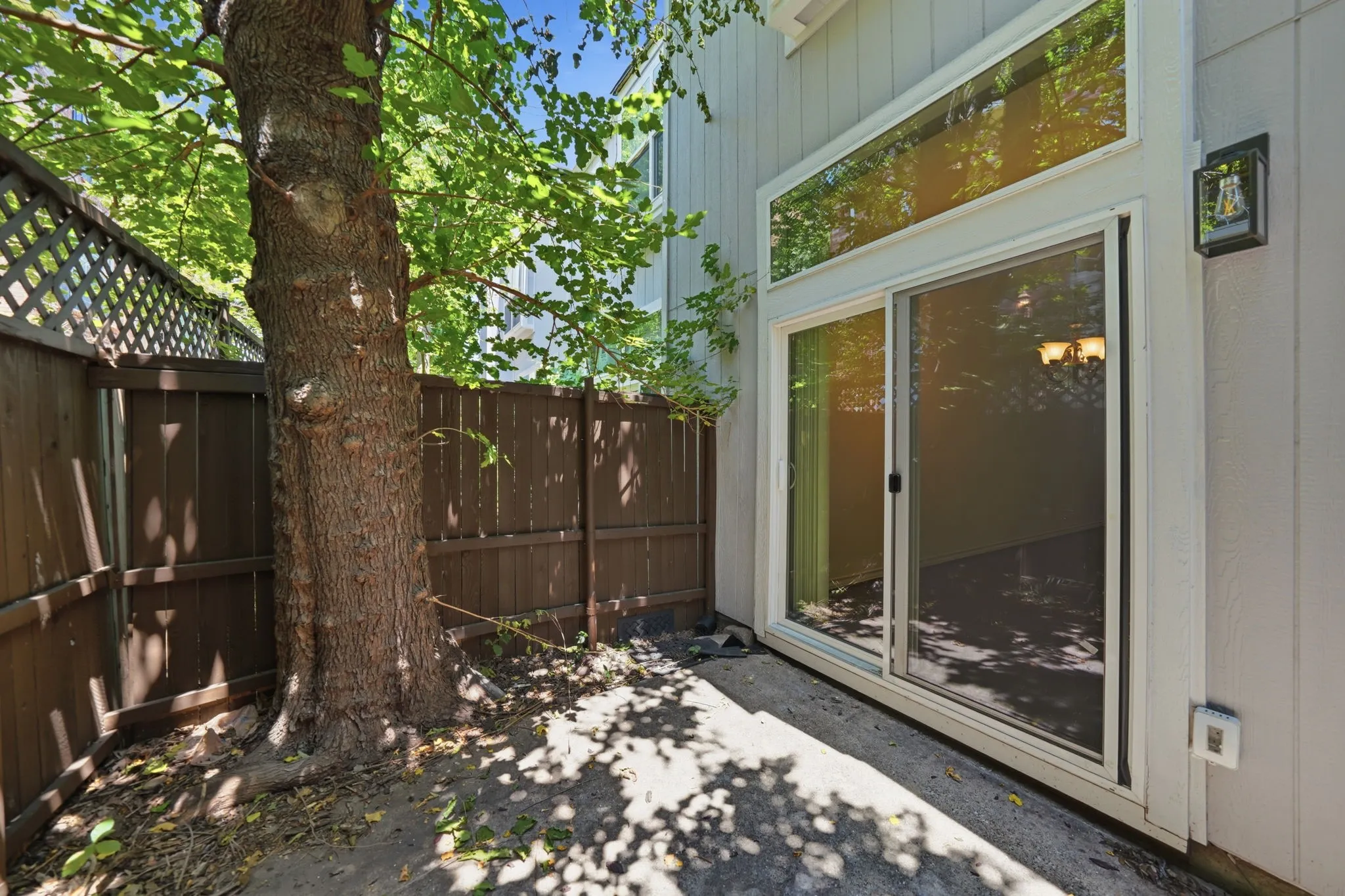 Private patio area featuring a mature tree, wood privacy fencing, and direct access to interior spaces via a sliding glass door
