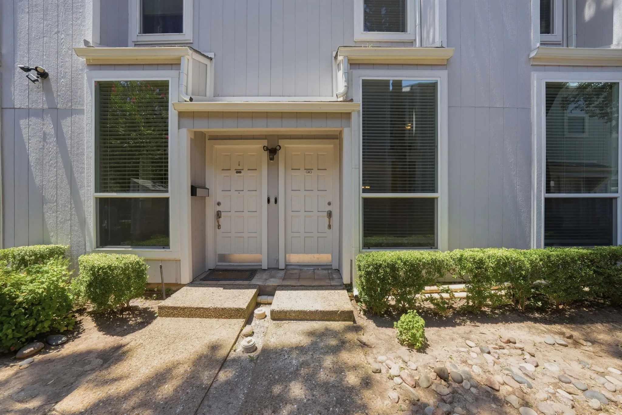 Light gray siding exterior with white trim accents and two entry doors featuring decorative paneling