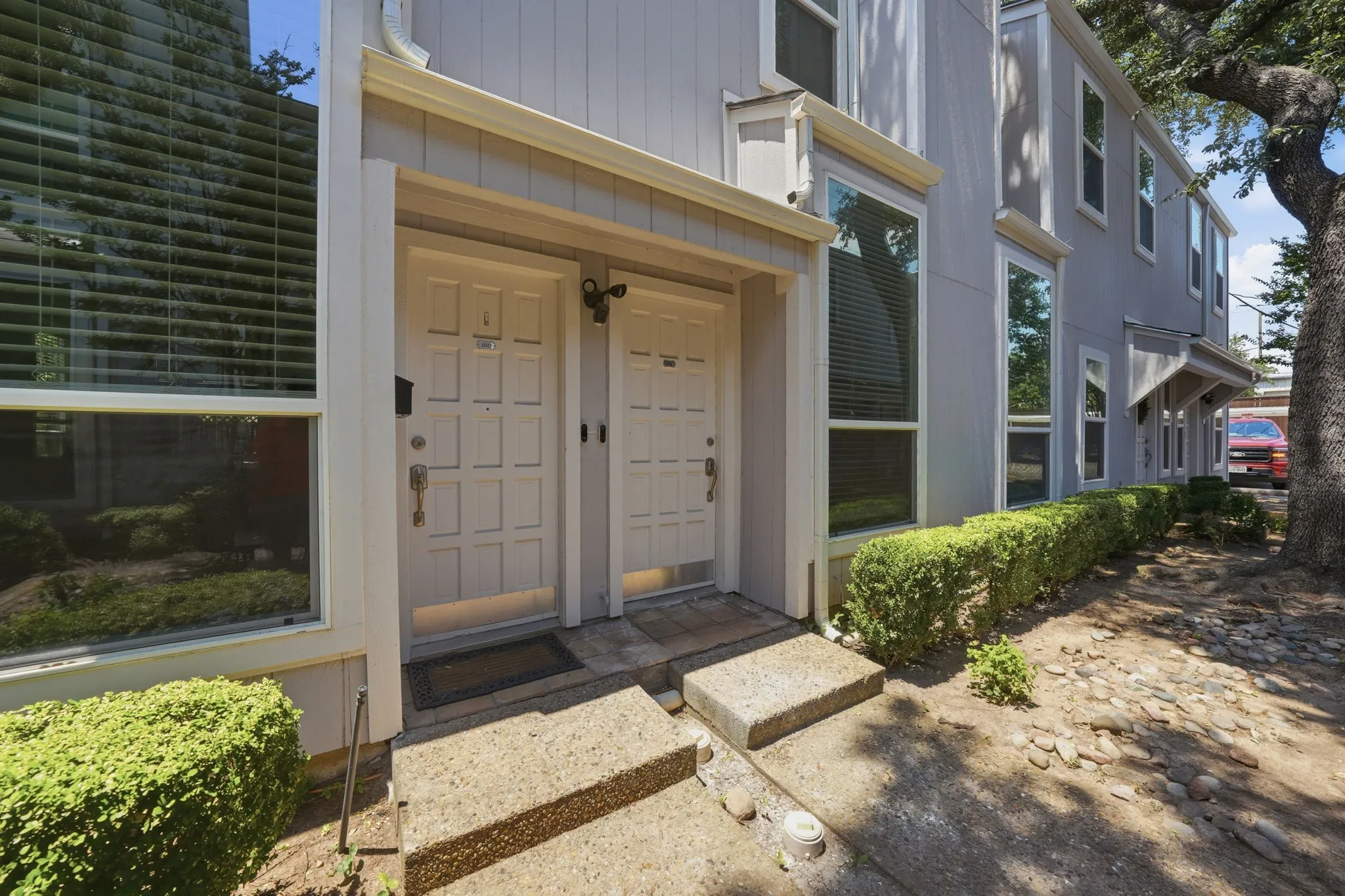 Multi-story facade featuring a light gray exterior, multiple large windows with blinds, and two panel-style entry doors