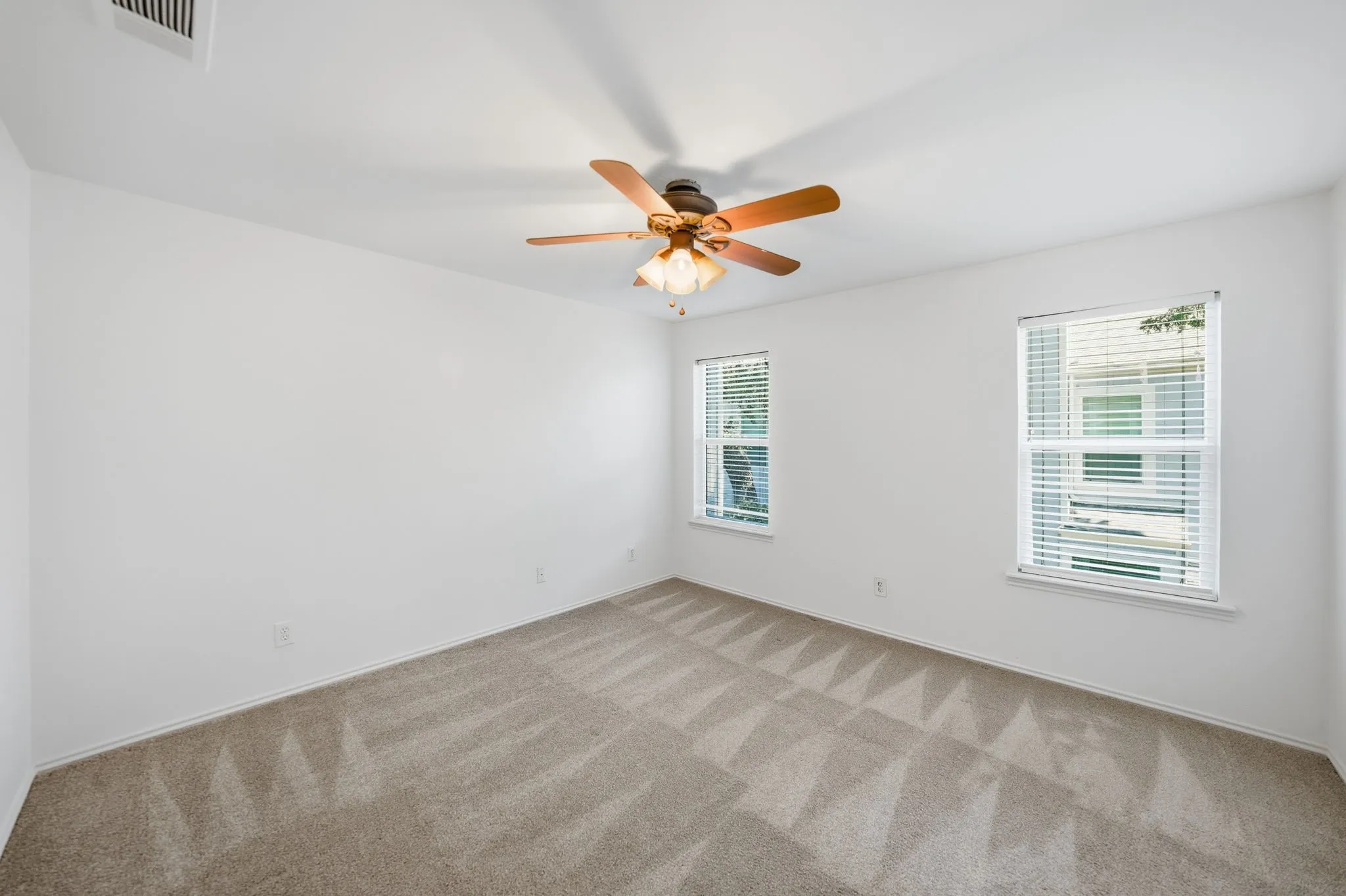 Carpeted room with a ceiling fan, two windows, and white walls
