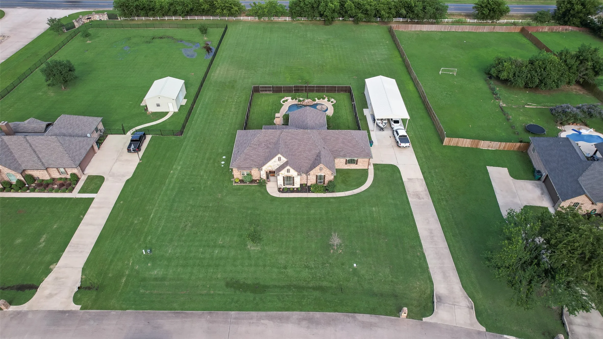 Expansive property featuring a brick exterior home, large green lawns, a detached two-car garage, a covered parking structure, and a fenced swimming pool area