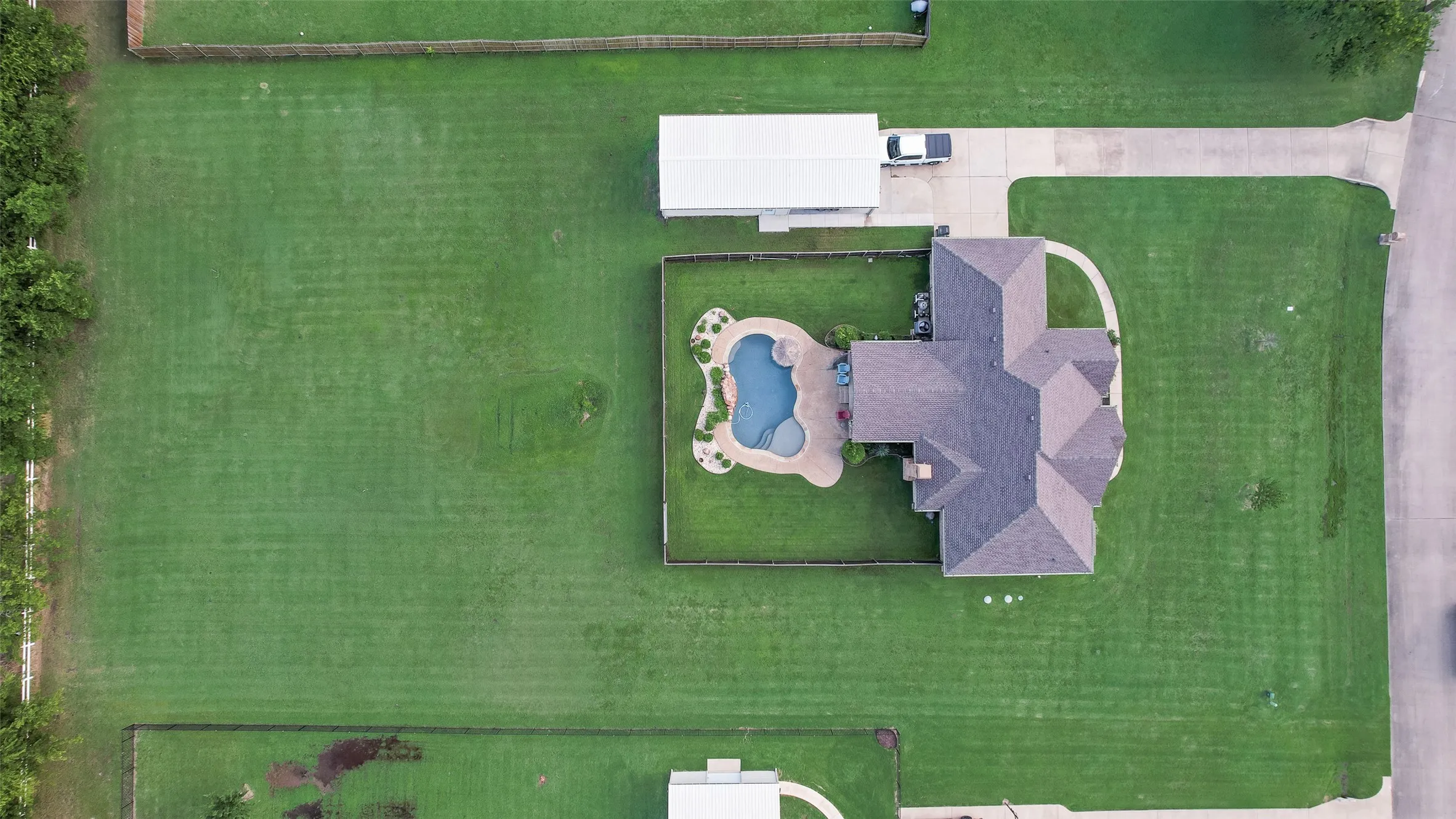 Spacious property featuring an irregular-shaped swimming pool with stone coping, mature trees, a detached carport, and extensive lawn areas