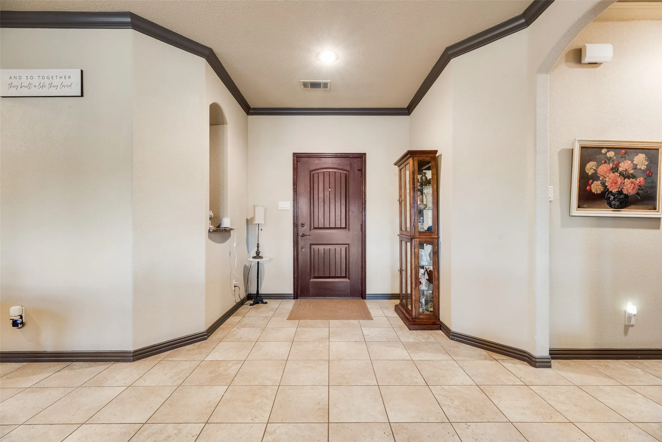 Entryway featuring light-toned tile flooring, a dark wood-finish entry door with paneling, and contrasting dark-stained crown molding and baseboards