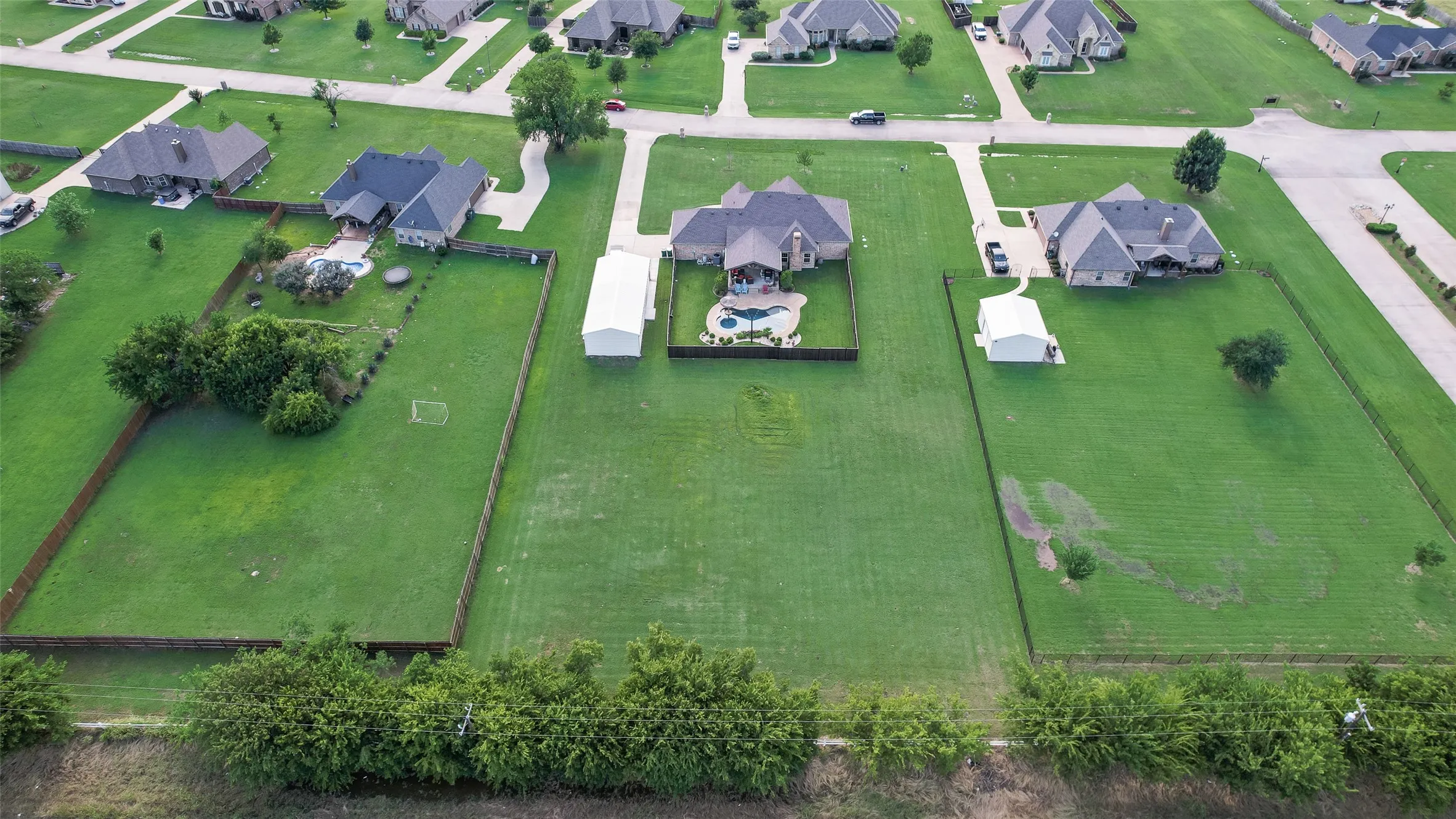 Expansive property featuring a single-family residence with a dark shingle roof, a curving driveway, and an outdoor swimming pool