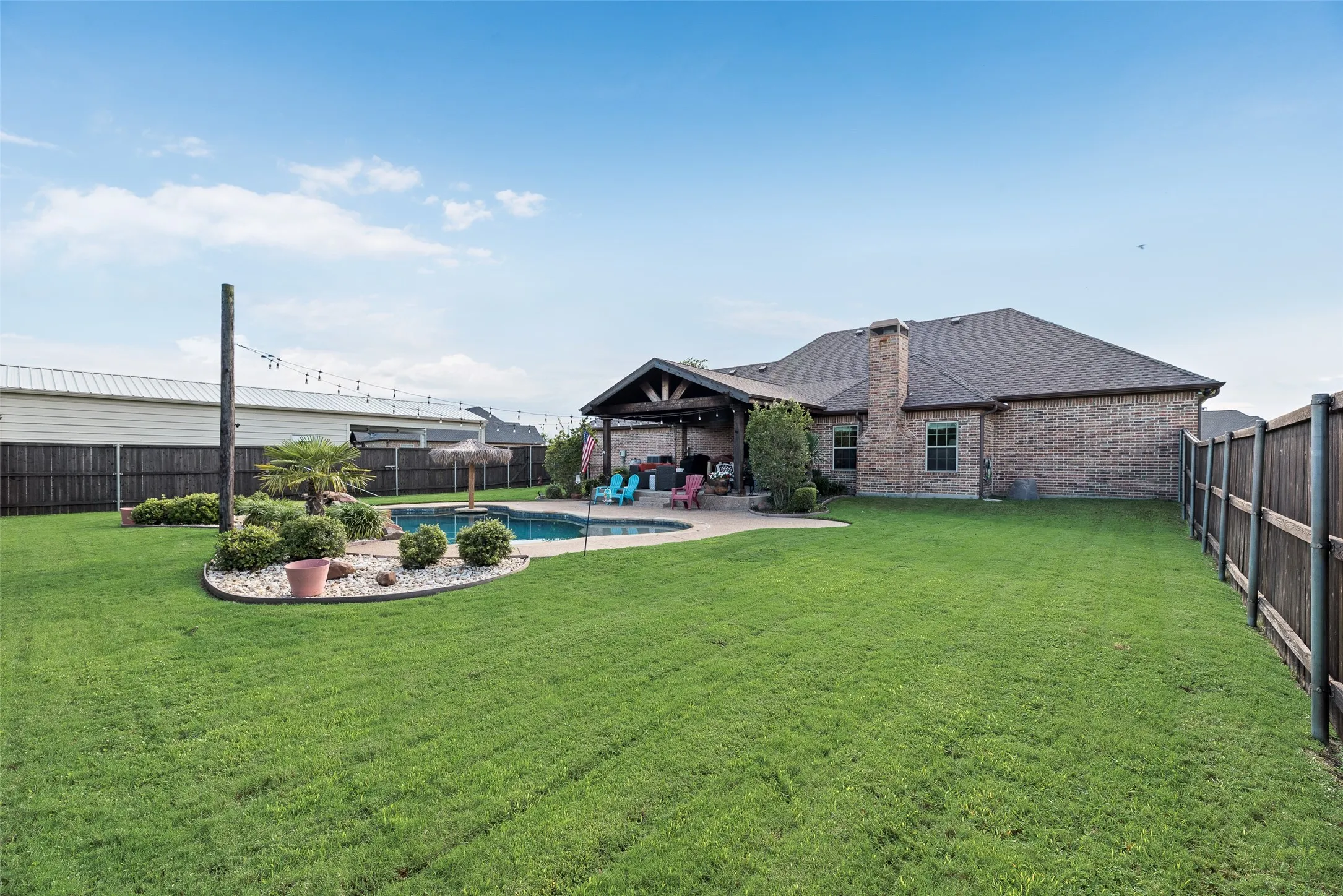 Expansive backyard featuring a gunite pool, a covered patio with exposed beams, and a brick-faced exterior
