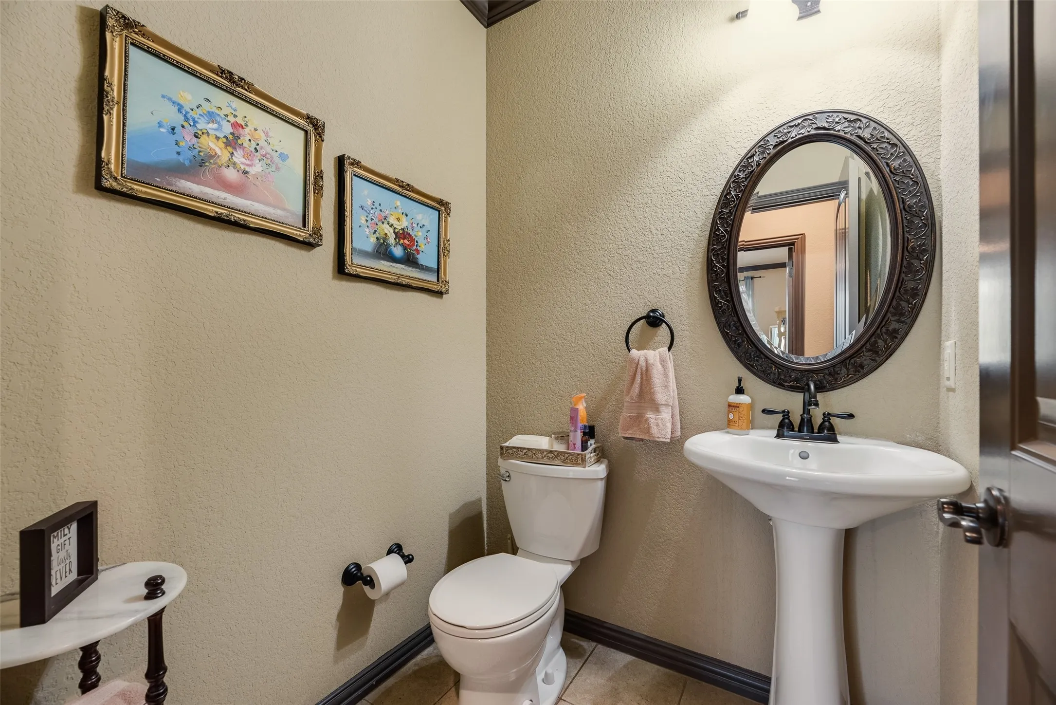Pedestal sink with dark-toned fixtures and an ornate oval mirror
