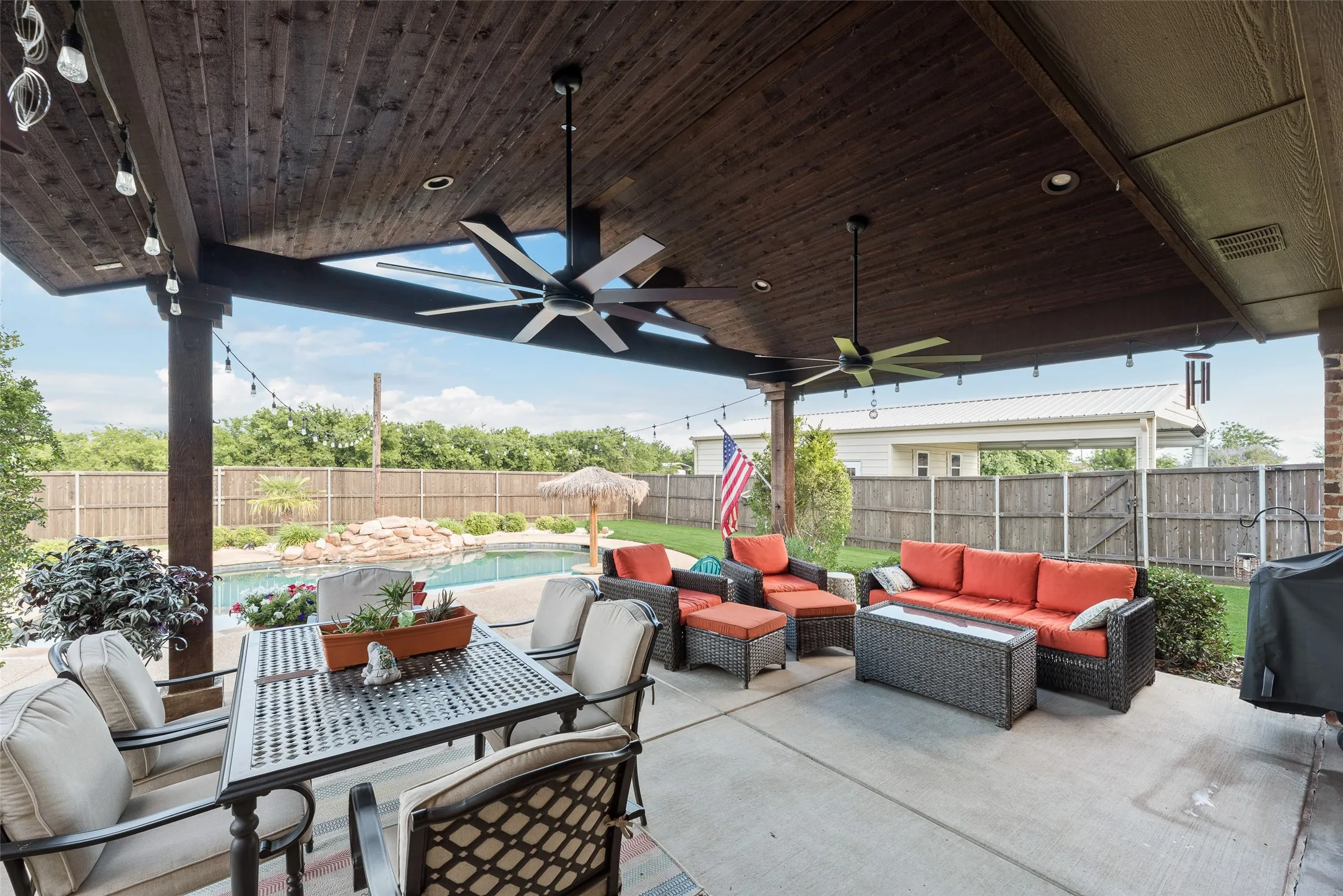 Expansive covered patio featuring a dark wood-finish ceiling, multiple ceiling fans, recessed lighting, and string lighting